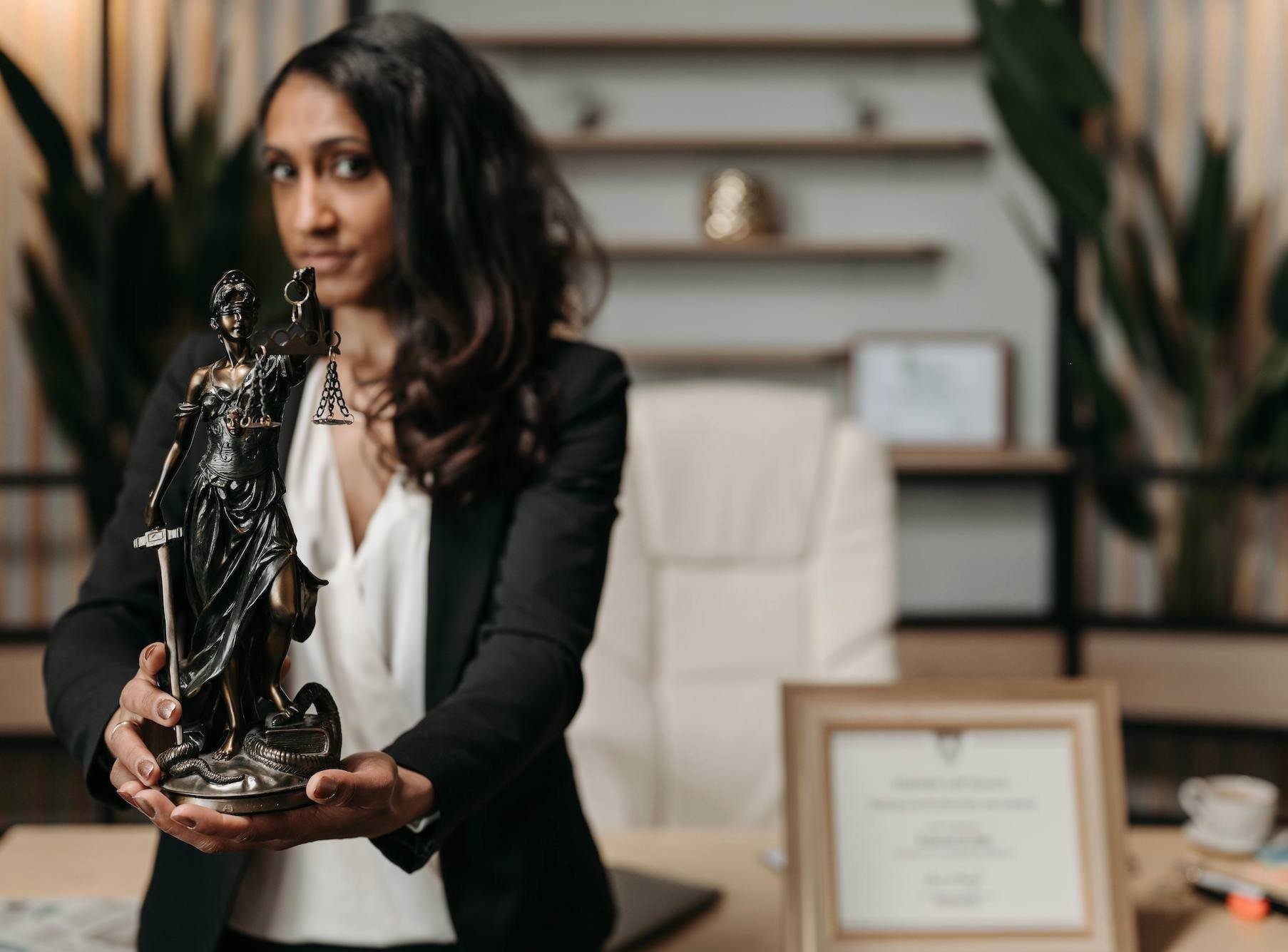 Woman holding a justice statue with a blurred office background.