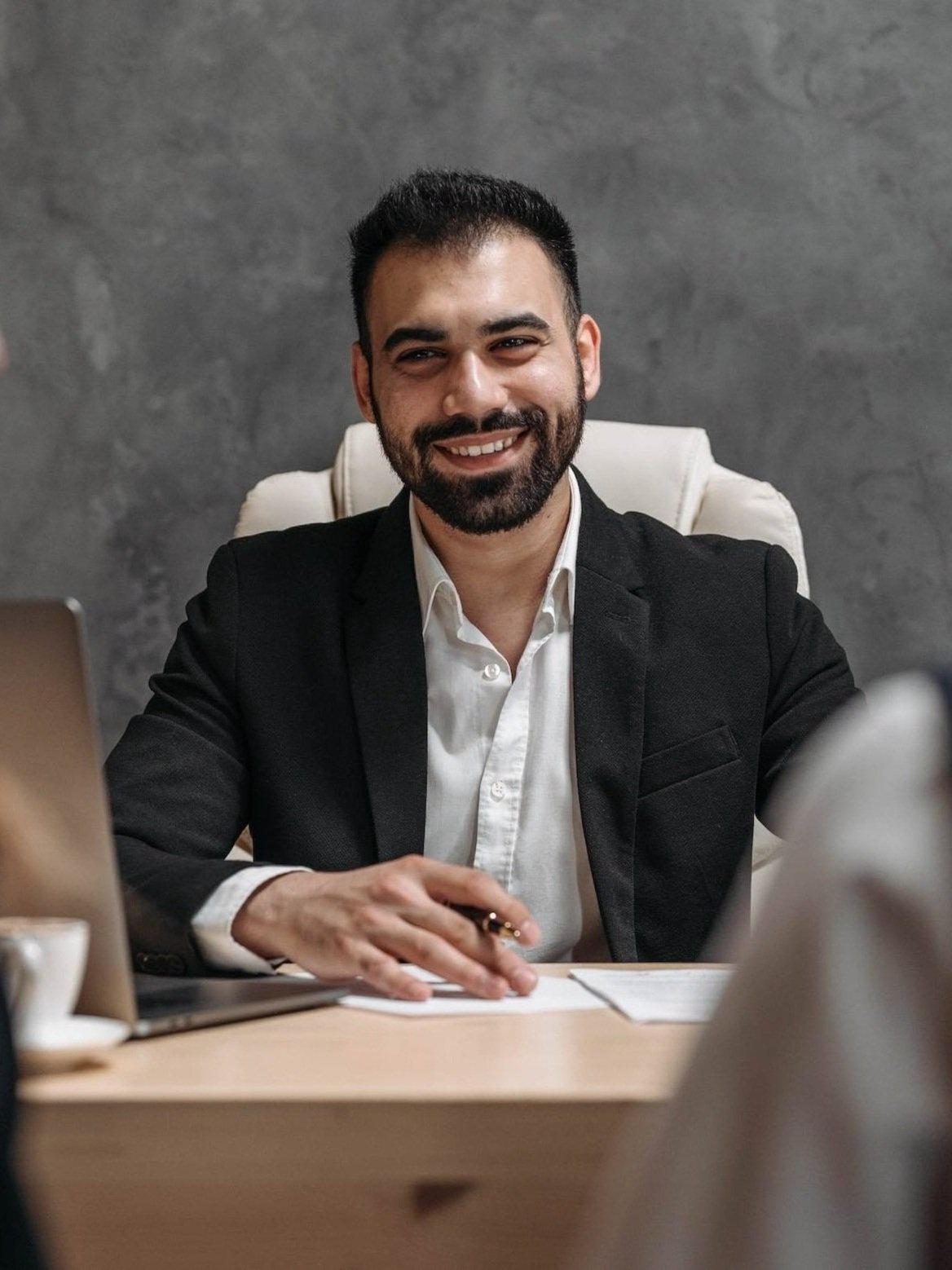 Businessman smiling, seated at a desk in an office setting.