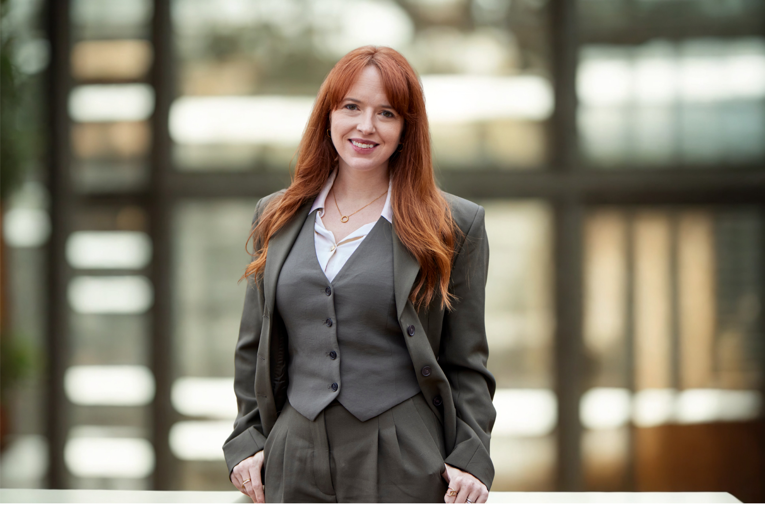 Mandy Conner, Principal Attorney at Conner Law Group,  standing with her hands in her pockets in an office or conference room with large windows and greenery outside.