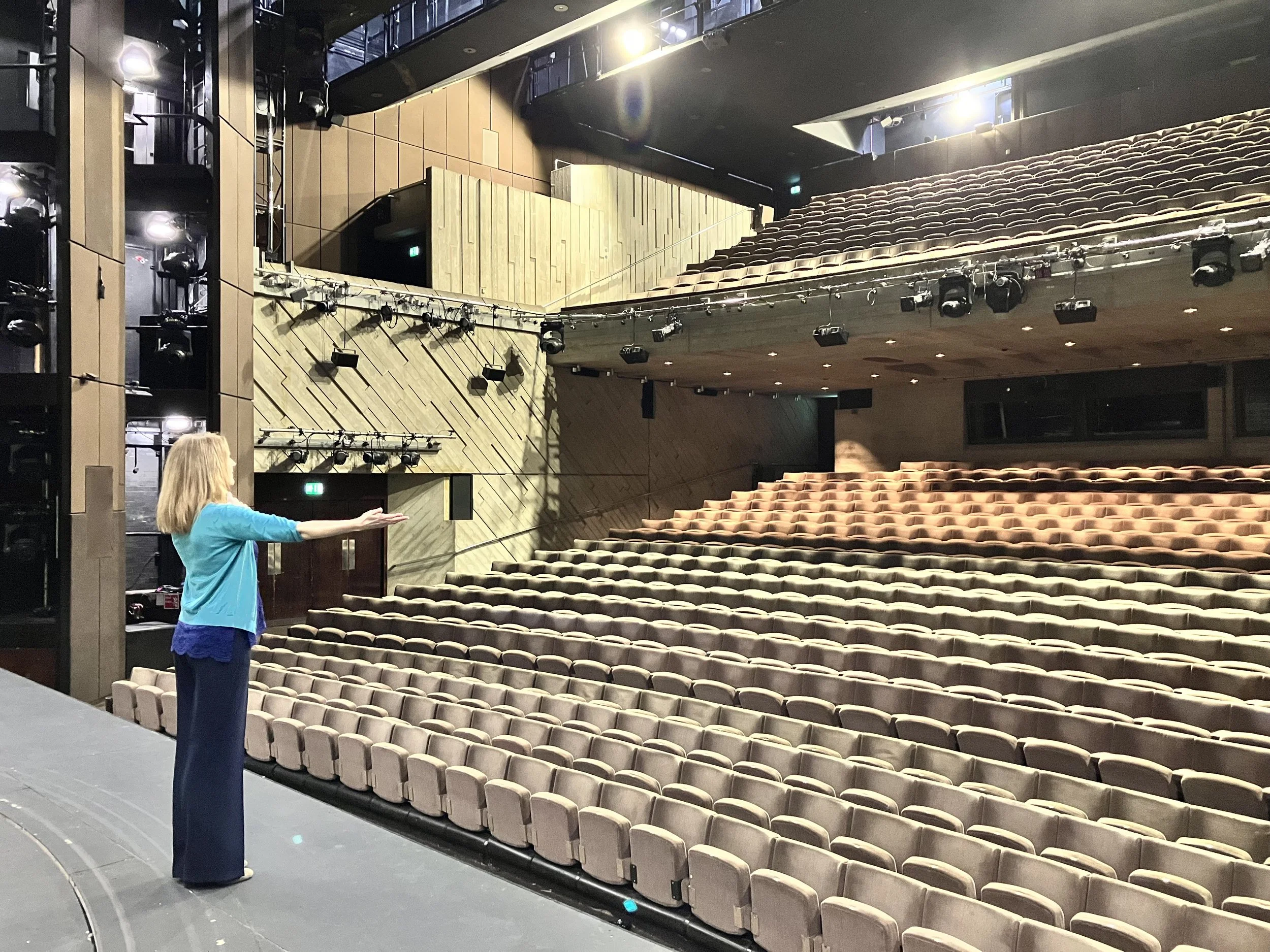 Liz Flint rehearsing on the Lyttleton Theatre stage at the National Theatre with empty seating and stage lights.