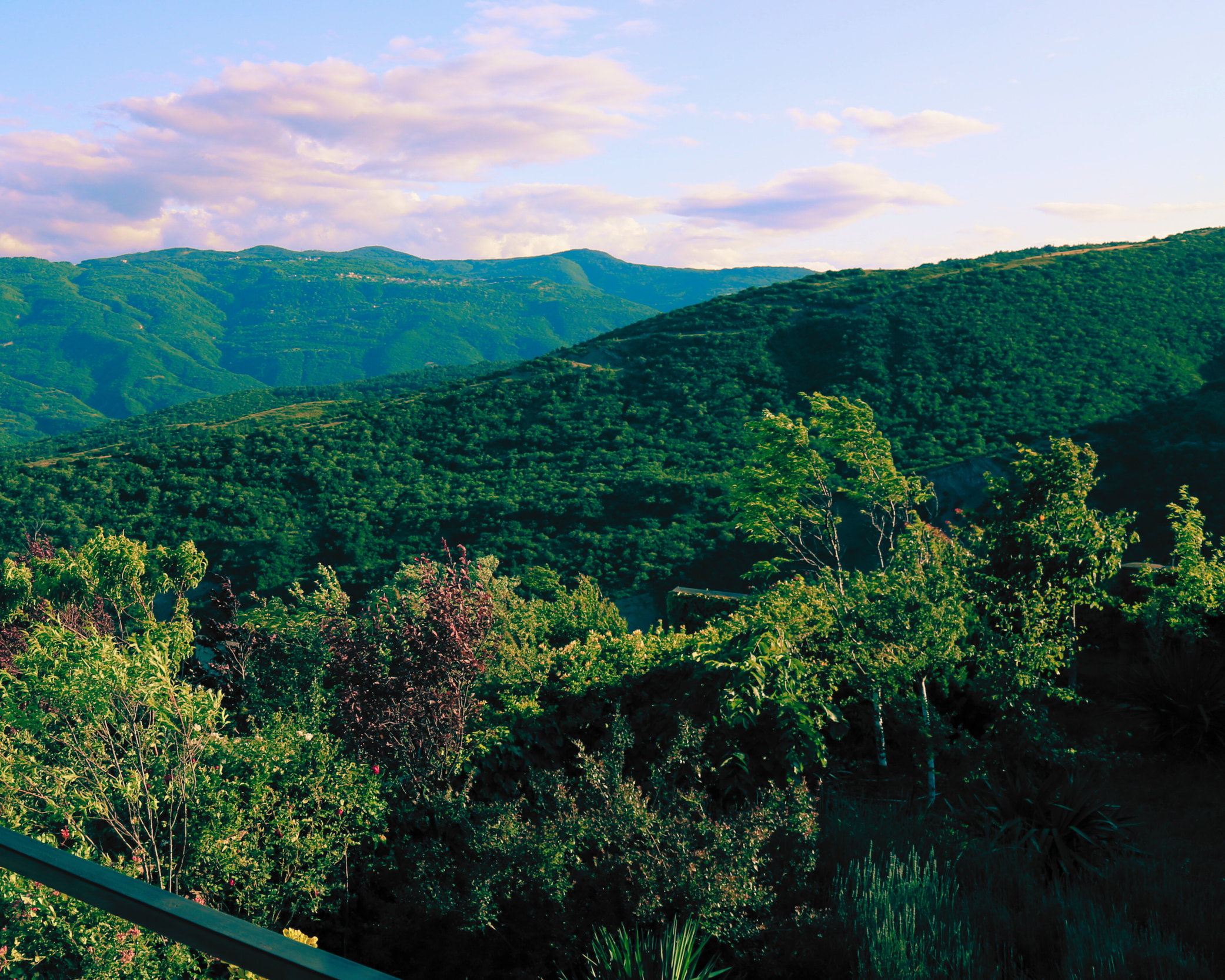Green mountainous landscape with lush trees and a cloudy sky.