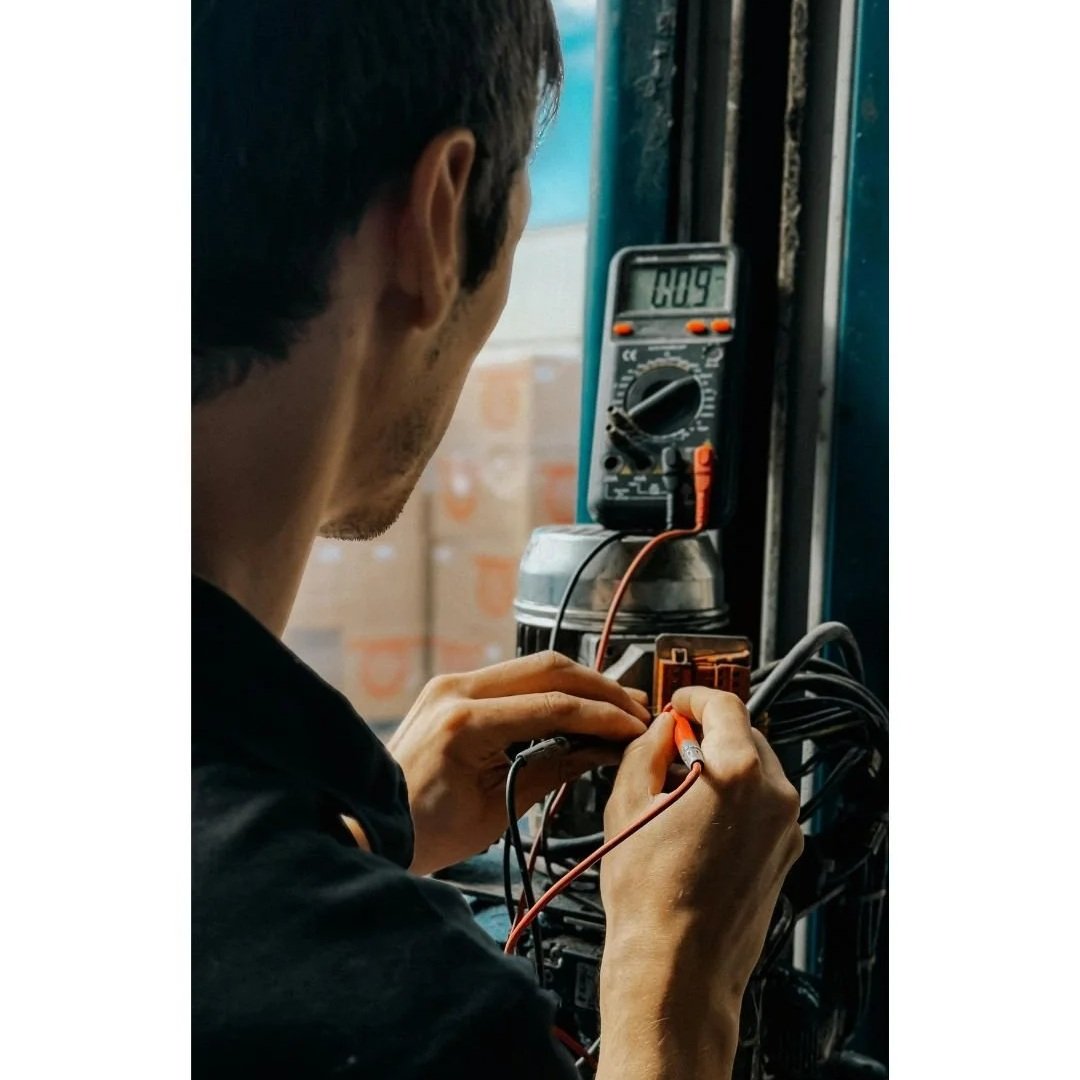 A person working with electronic devices on a blue workbench, using a digital multimeter to measure current or voltage.