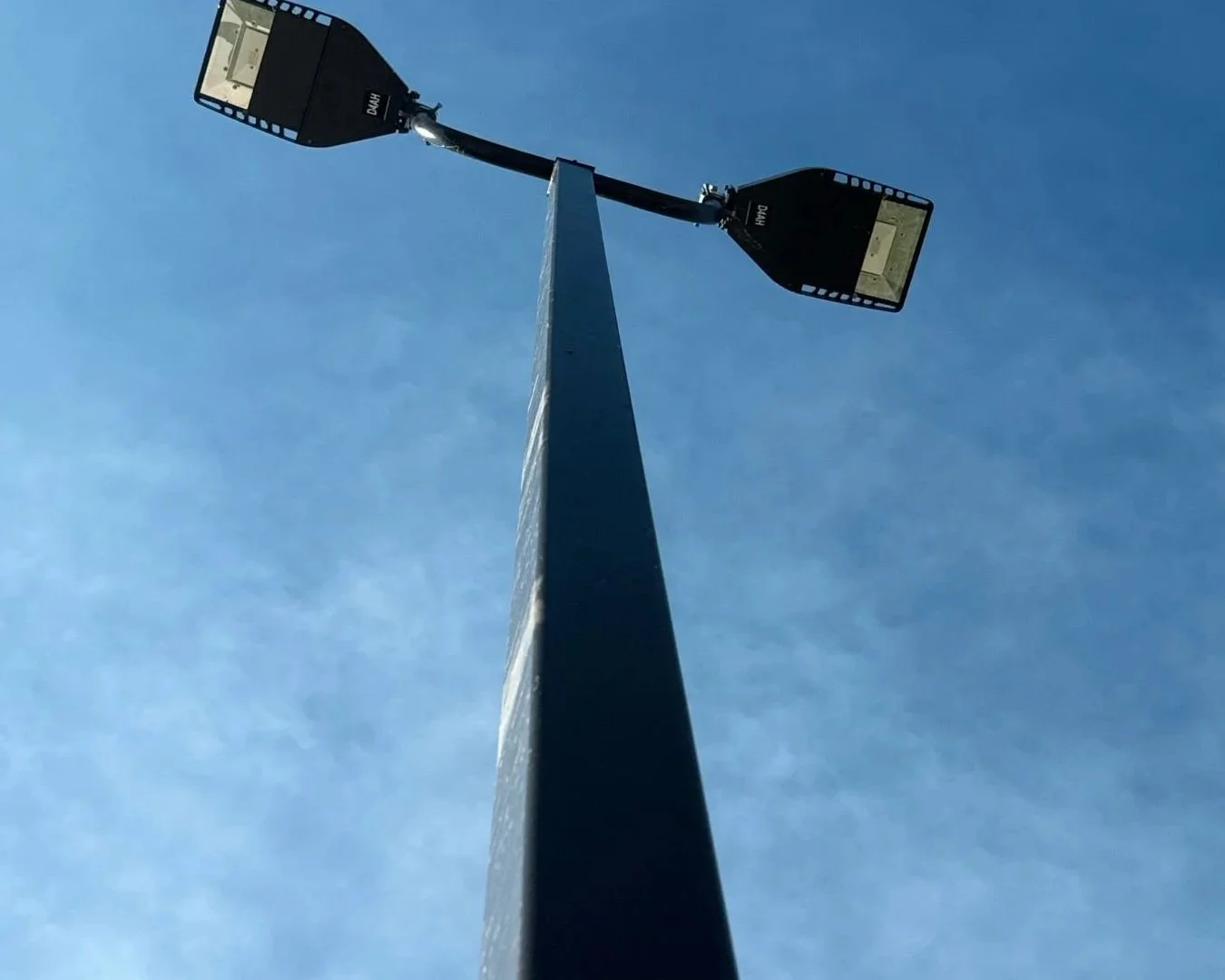 A tall streetlight pole with two floodlights against a blue sky.