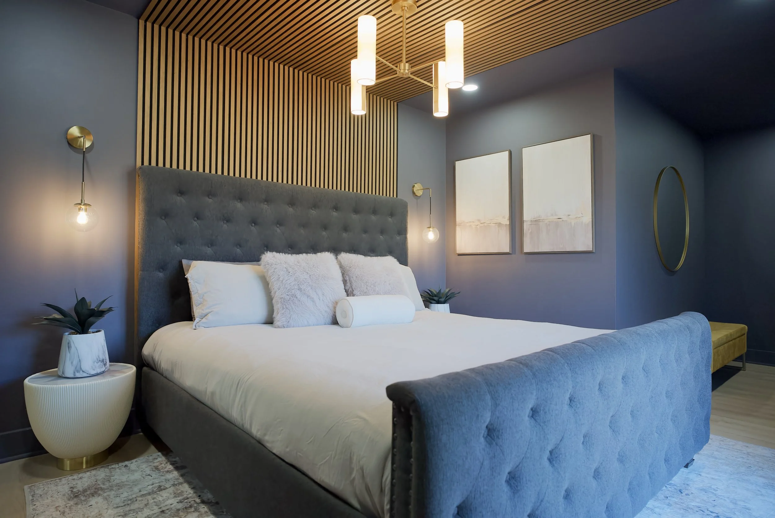 Unwind in a serene, designer-crafted bedroom featuring a plush king bed with premium linens and layered comfort. Elegant gold-accent lighting and a custom wood-slat ceiling create a warm, upscale ambiance.

Enjoy a wall-mounted TV, natural light from