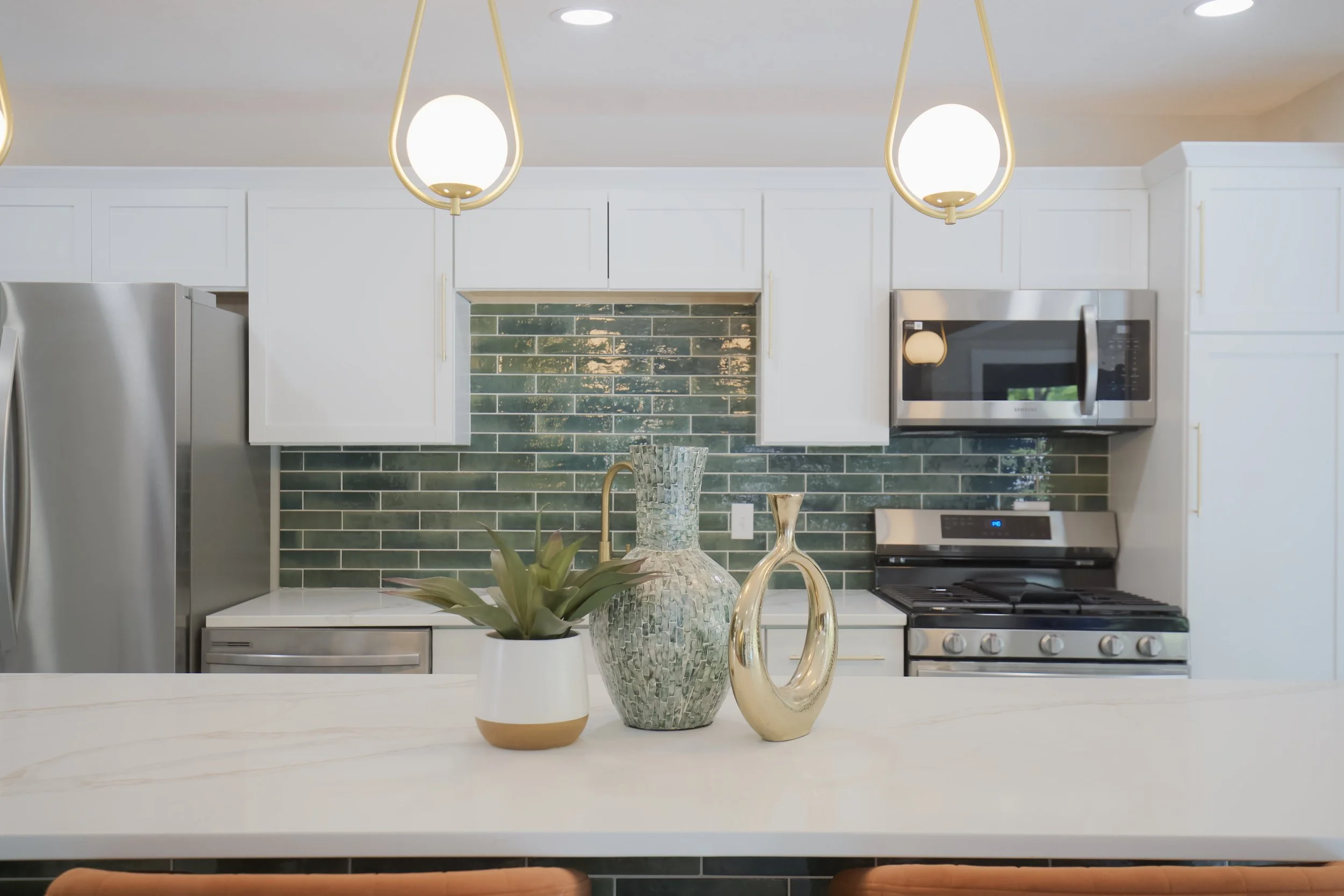 Modern kitchen with white cabinets, green tiled backsplash, stainless steel appliances, and decorative vases and plant on the counter.