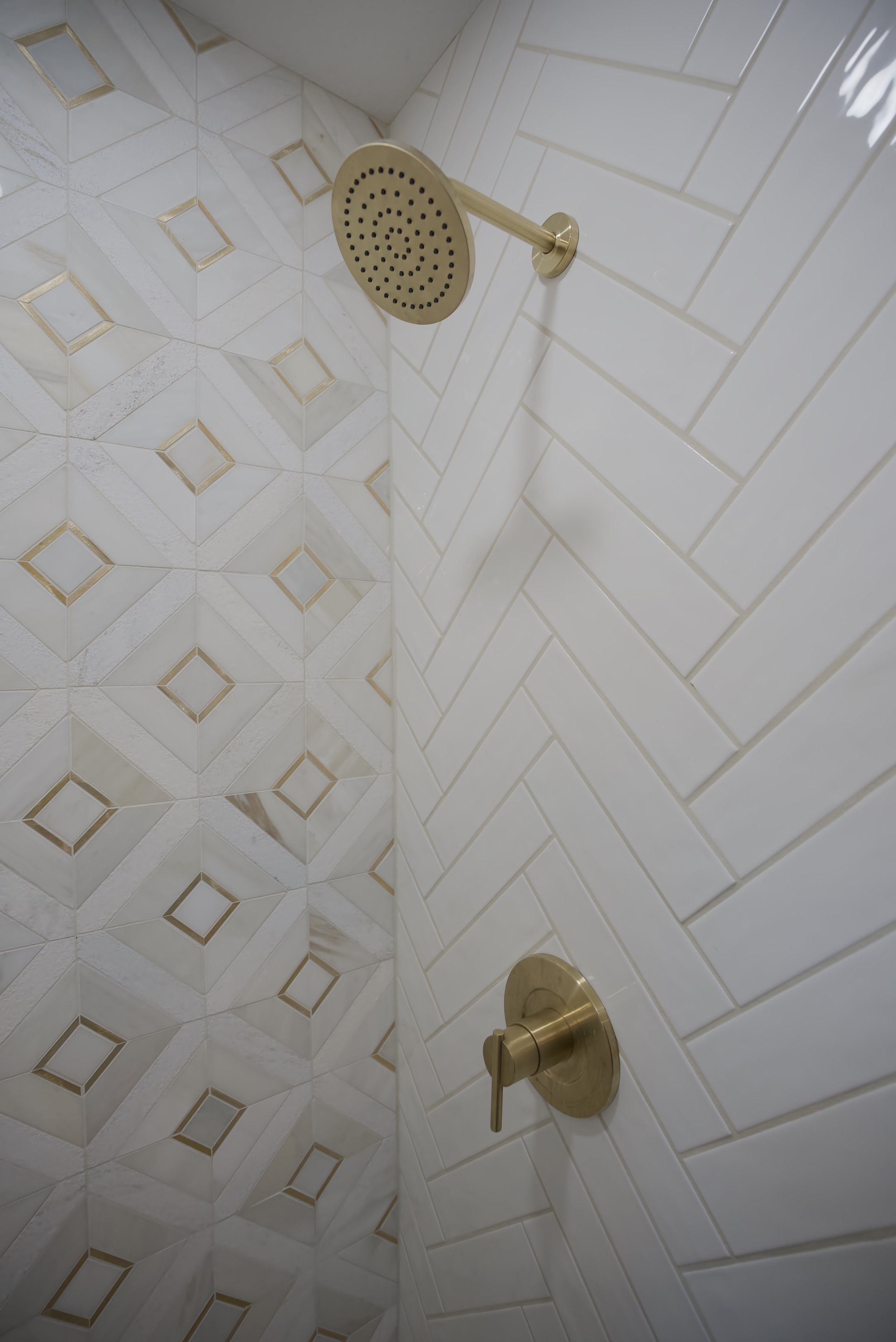 Close-up of a showerhead and a shower control handle mounted on a tiled wall in a bathroom shower.
