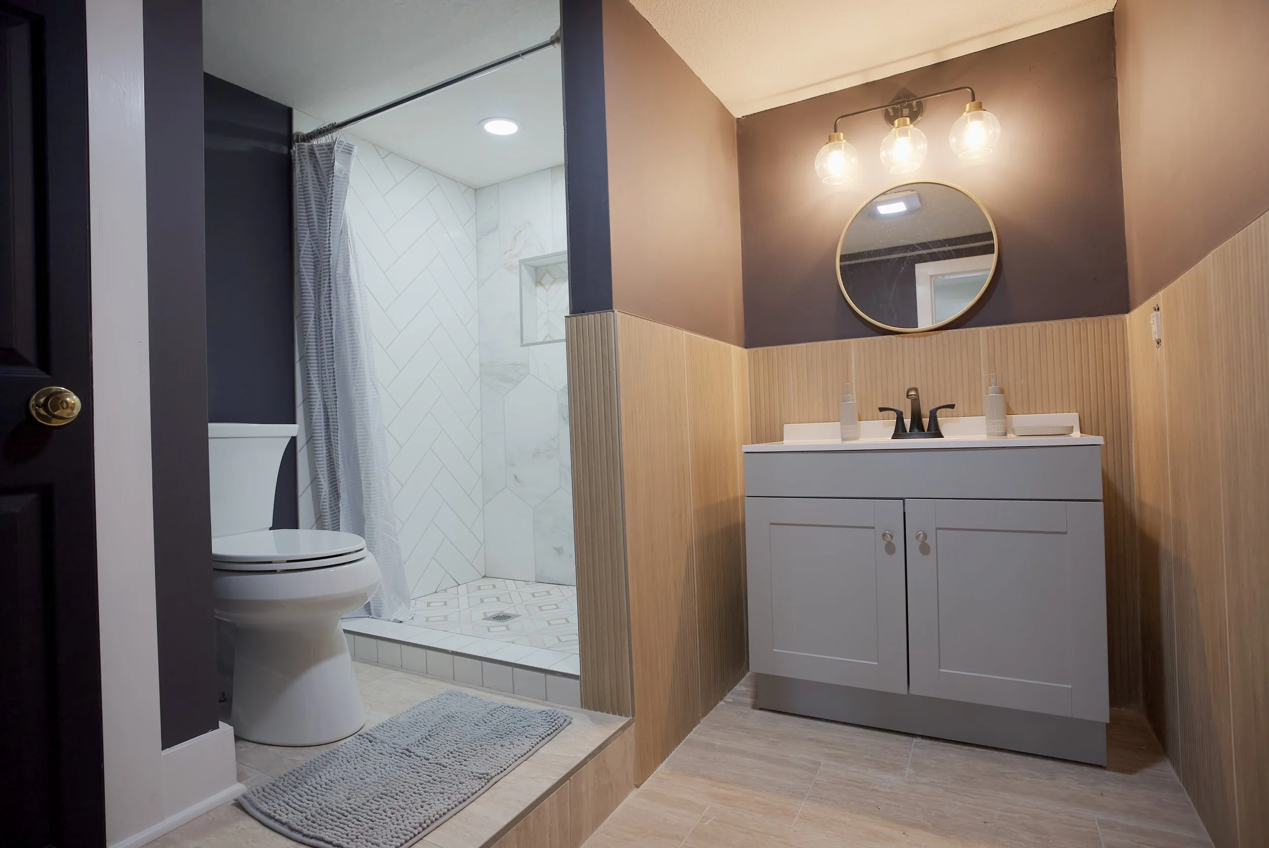 Bathroom with a shower area, toilet, and vanity with mirror and light fixtures.
