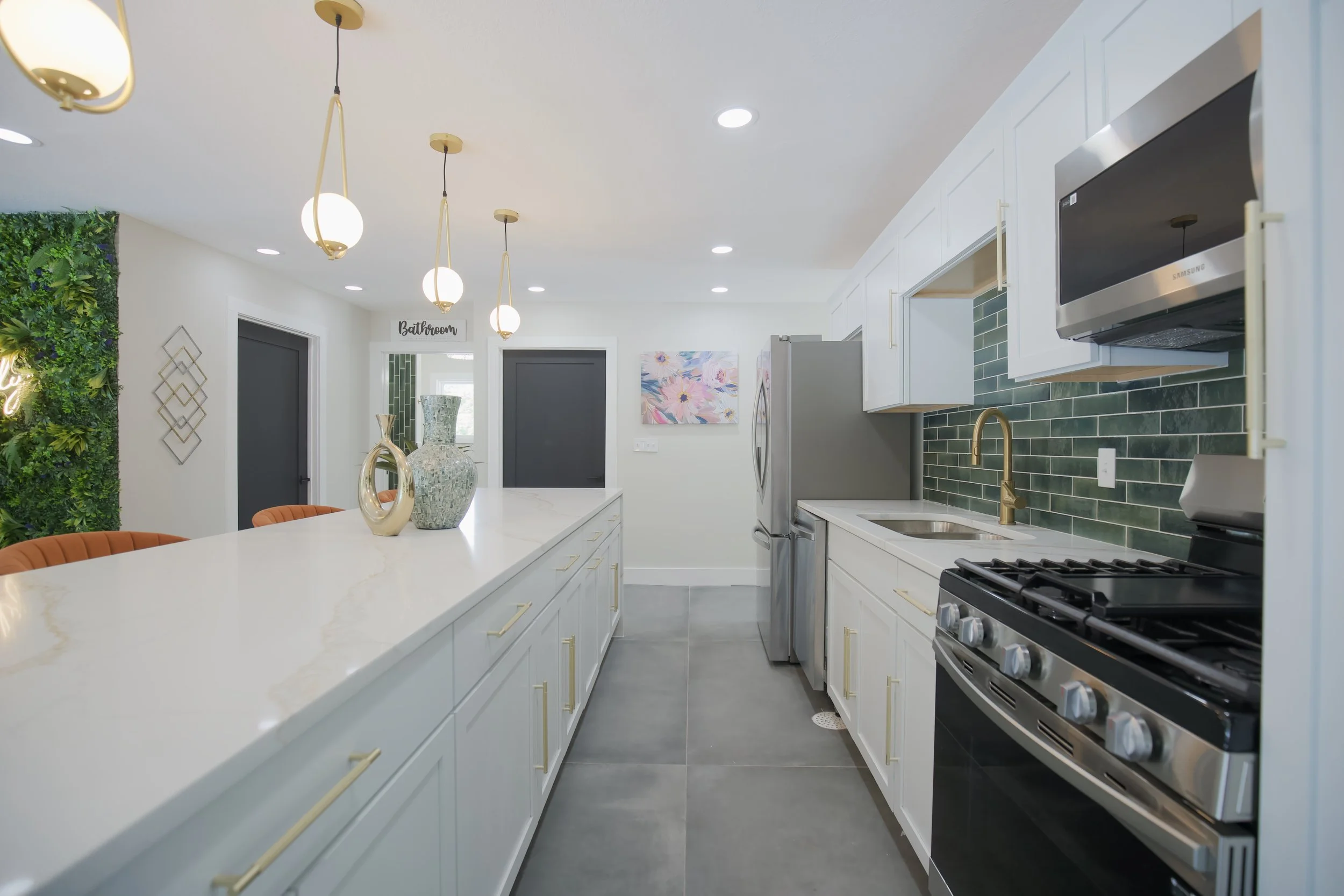 Modern kitchen with white cabinets, green tile backsplash, stainless steel appliances, and pendant lighting, with decorative vases on a white countertop.