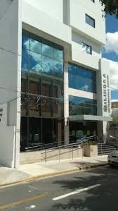 Fachada de um edifício moderno com janelas de vidro e portas de vidro na entrada, localizado na rua com estacionamento em frente.