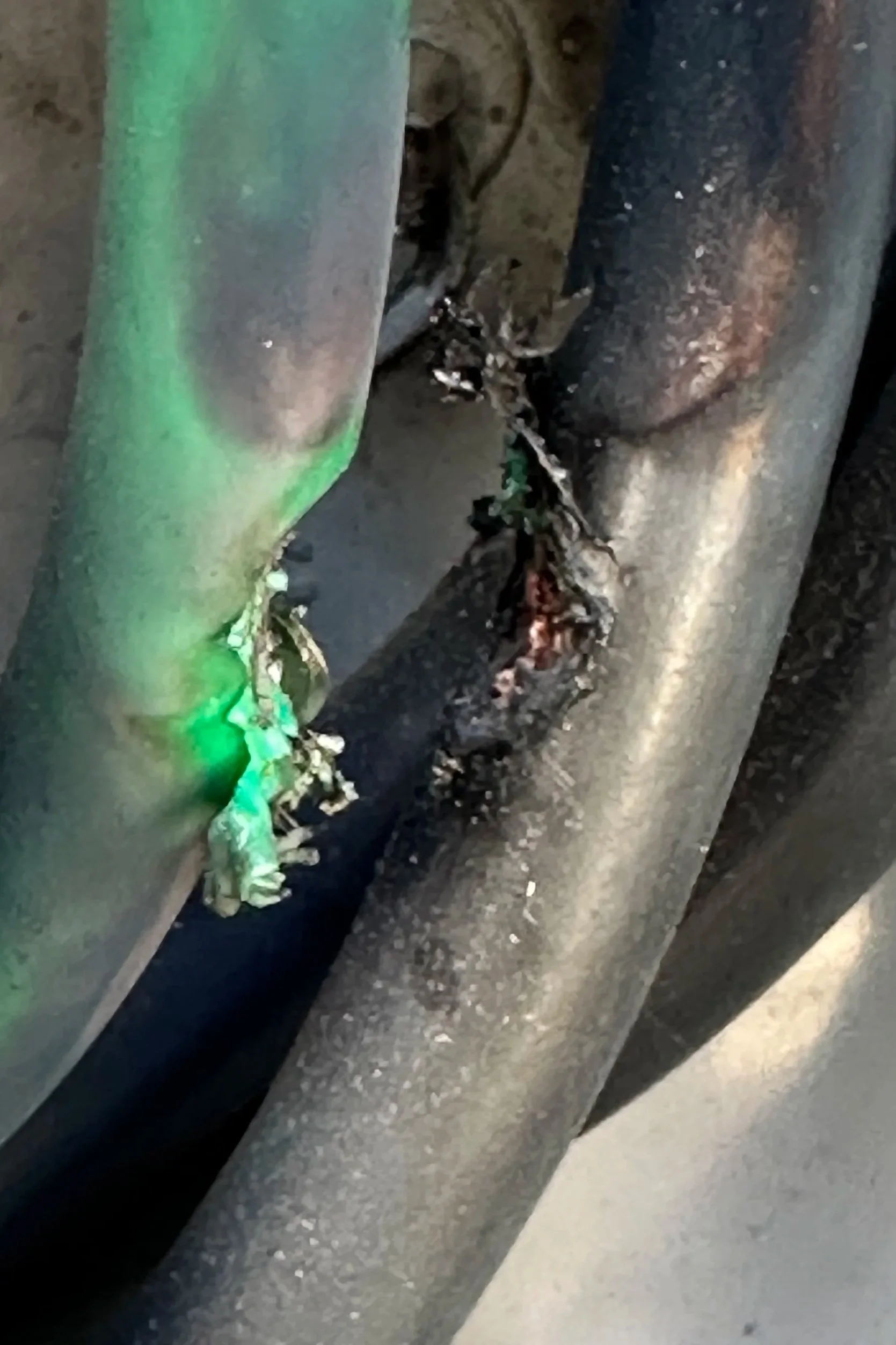 Close-up of a metallic pipe with some green paint, rust spots, and debris around it.