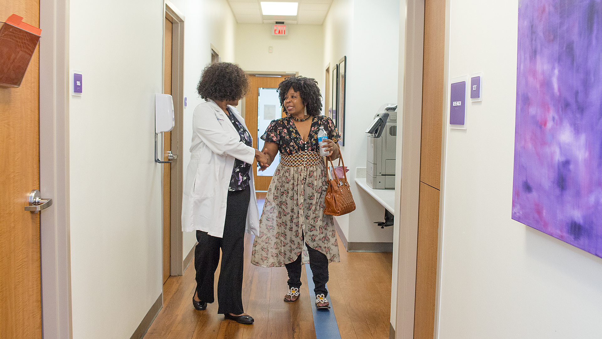 A PHNTX provider is shaking hands with a female patient in a hallway of PHNTX South Dallas Health Center.