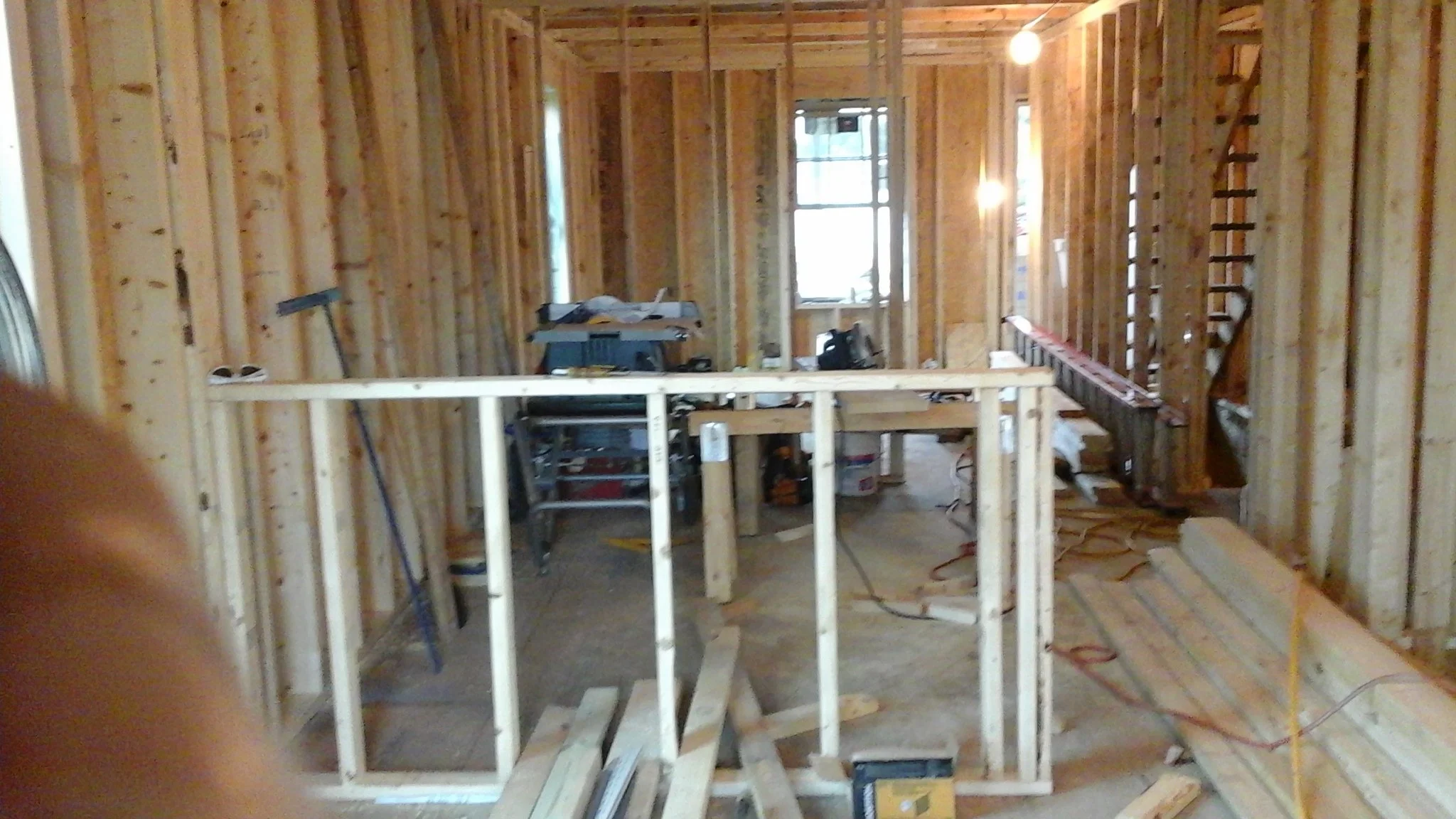 Interior of a house under construction, with exposed wooden framing, construction tools, and materials scattered around.