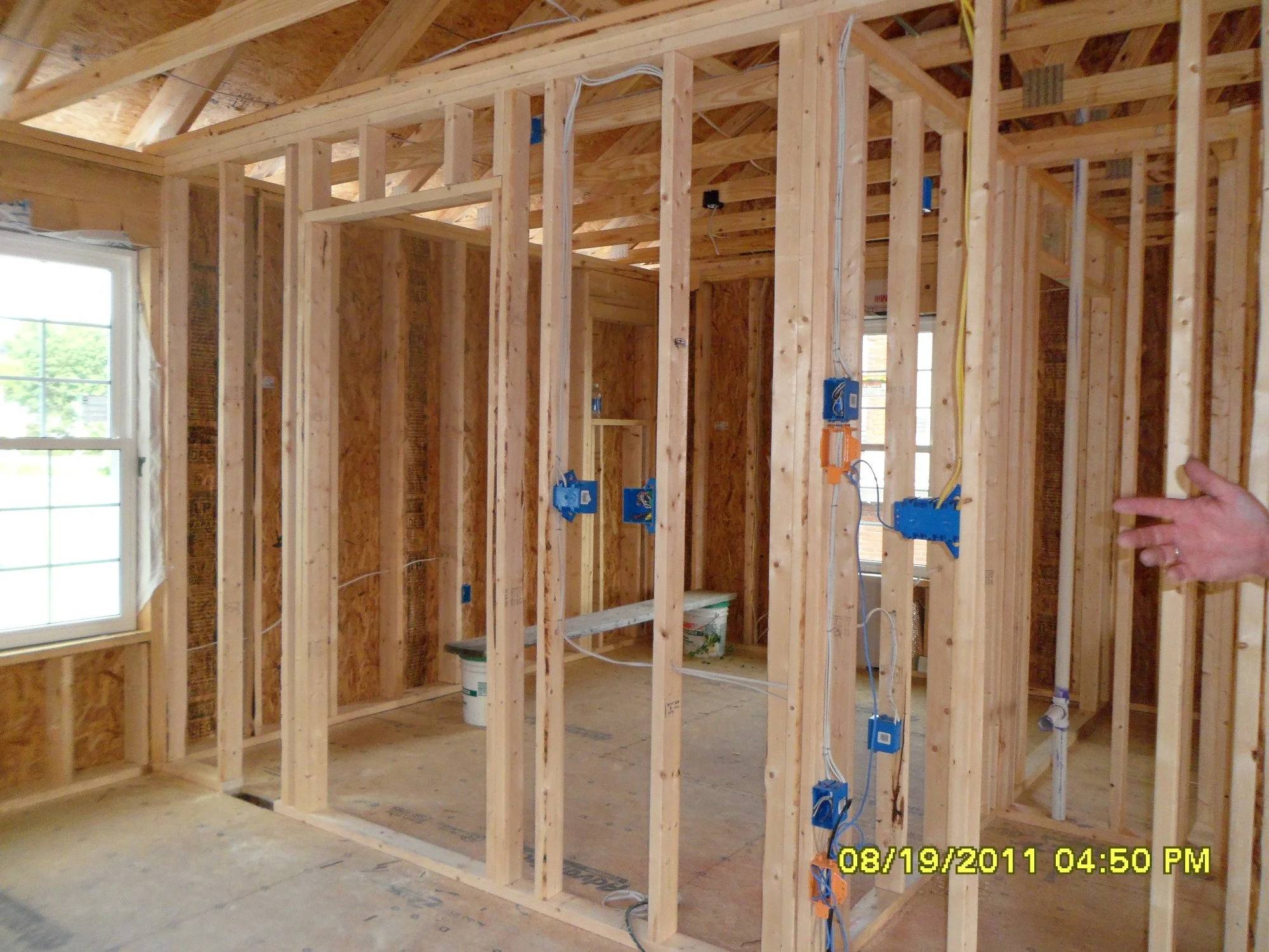 Interior view of a house under construction, showing exposed wooden framing and electrical wiring.