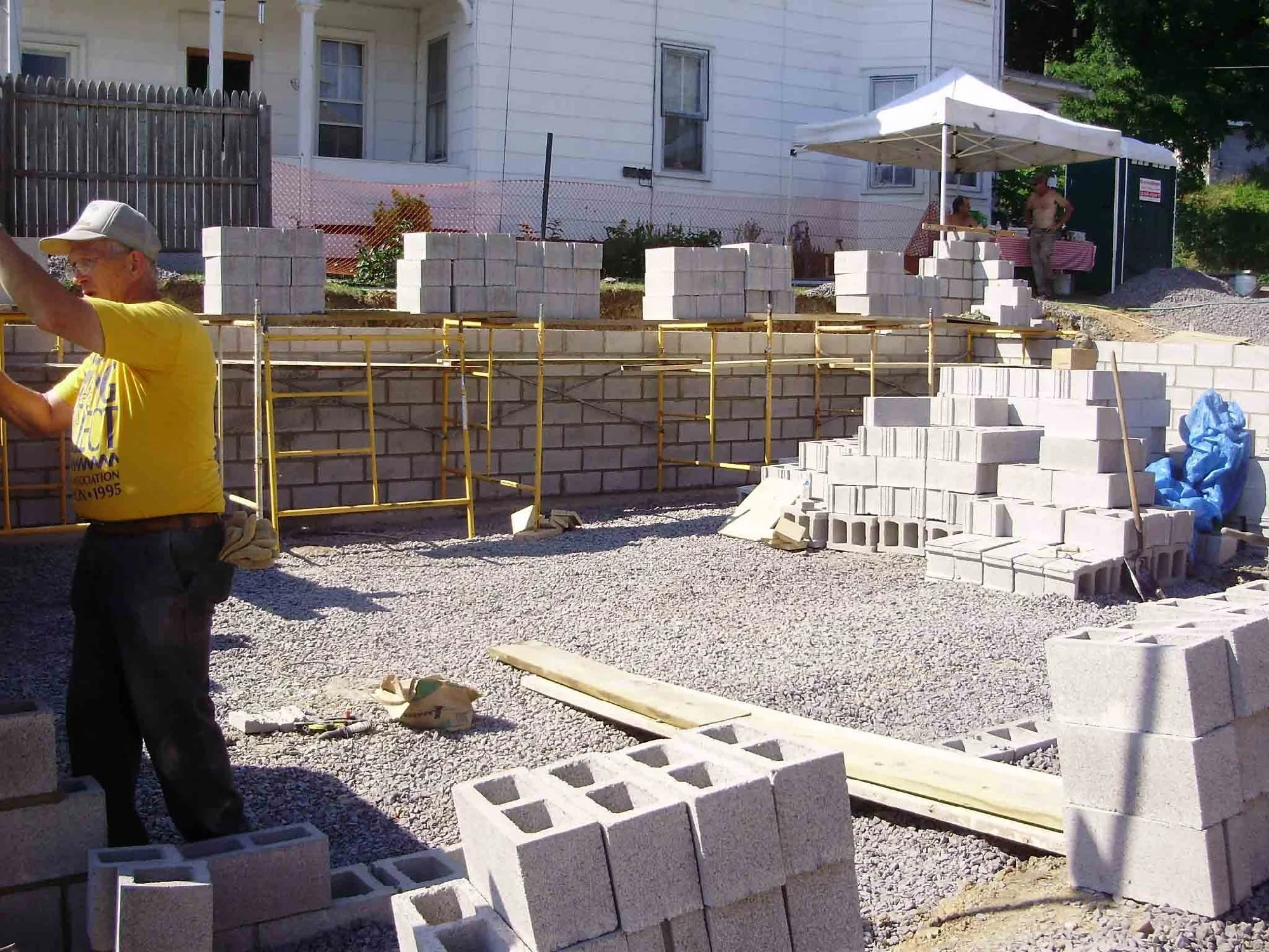 Construction workers building a brick wall on a residential property with scaffolding and cinder blocks.
