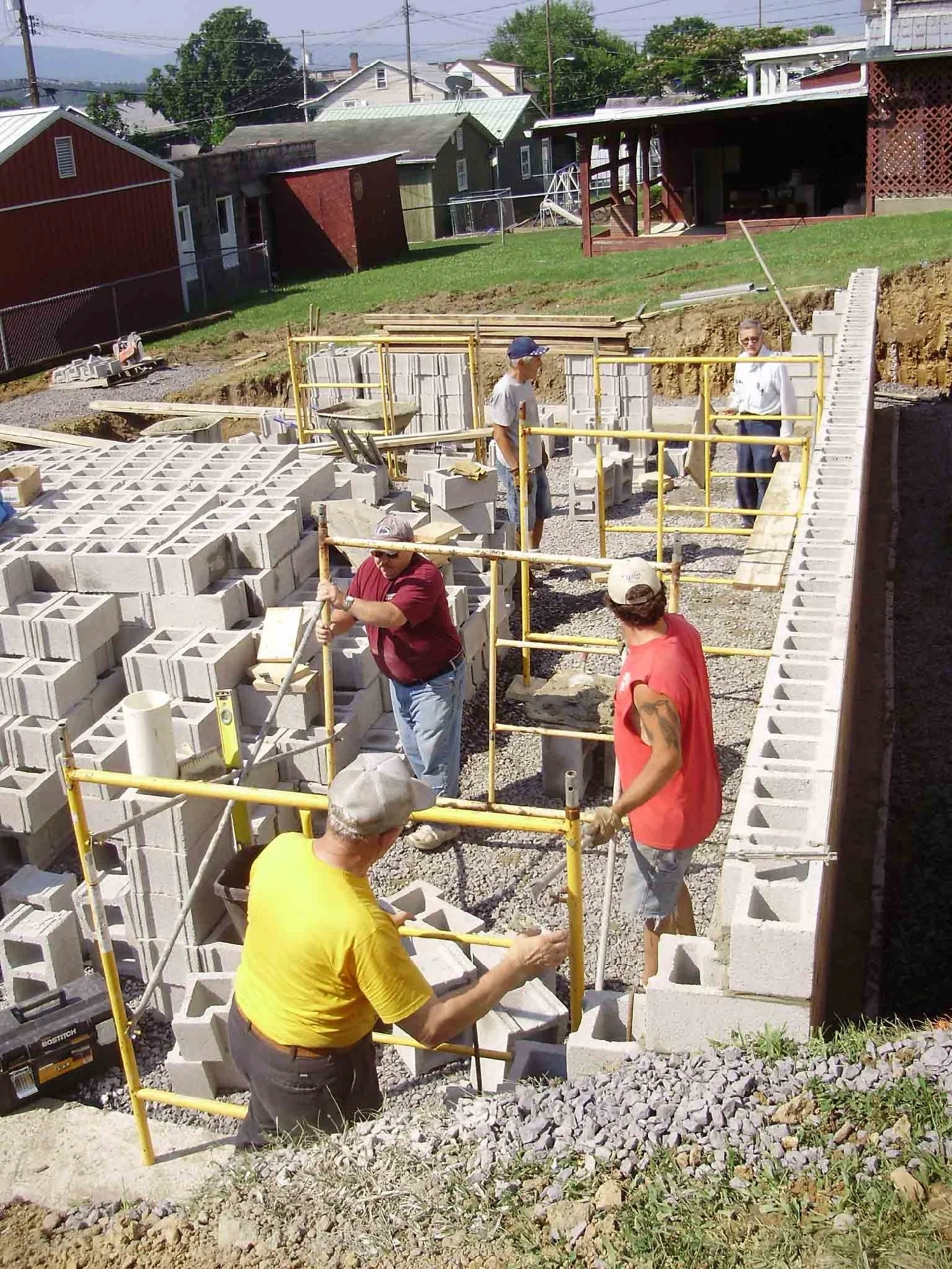 Construction workers building a basement wall using concrete blocks, with some workers laying blocks and others working on scaffolding.