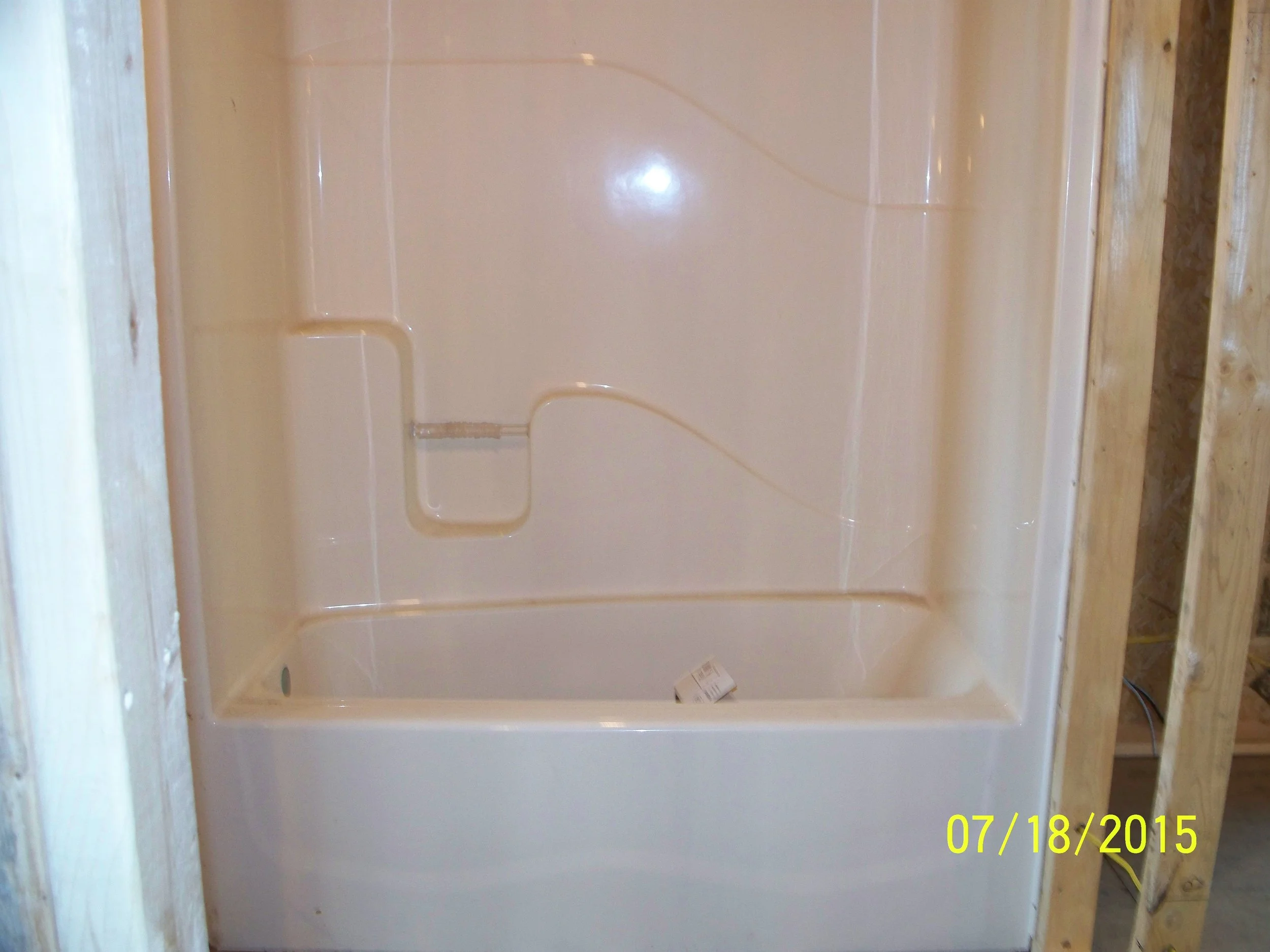New white bathtub installed in a bathroom under construction, with exposed wooden framing around it, and a date stamp of July 18, 2015.