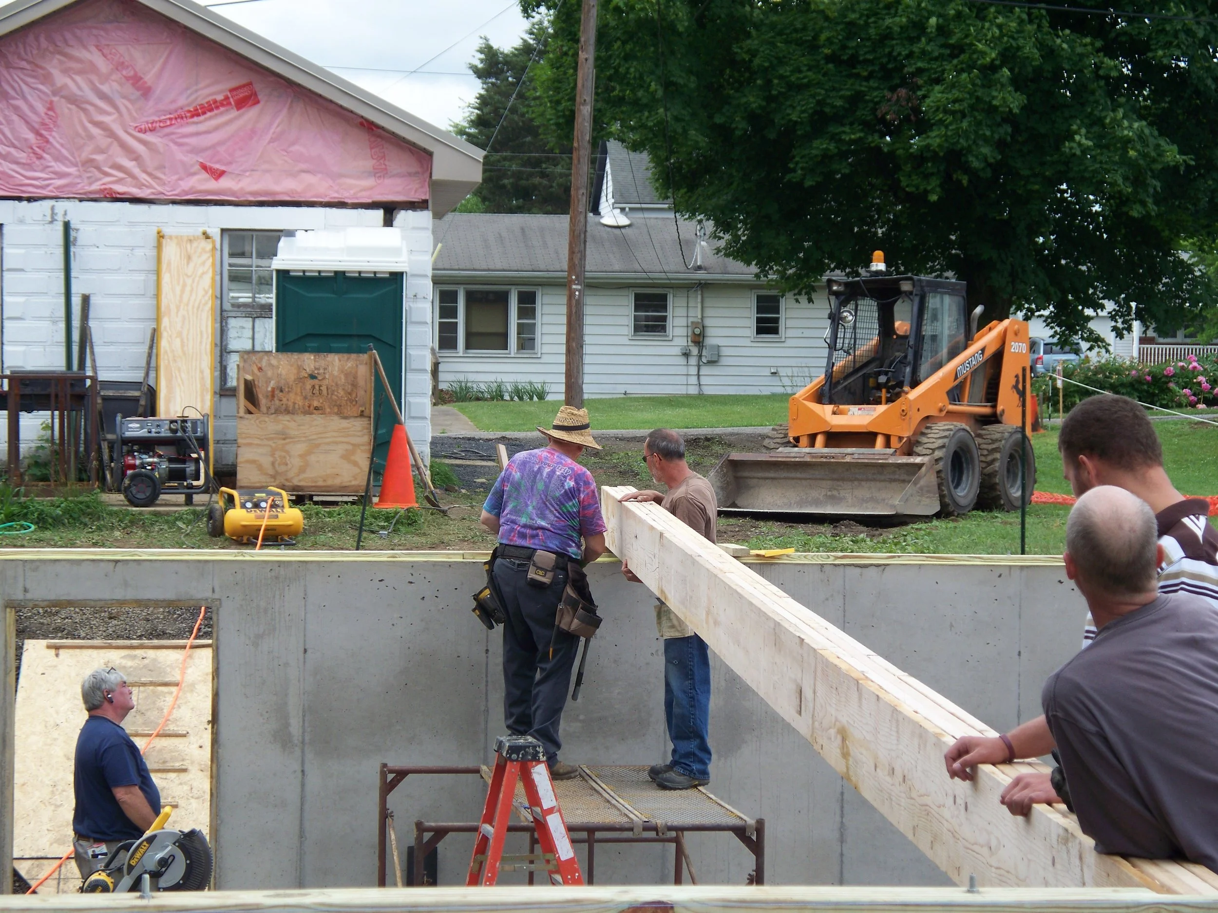 Construction workers building a structure with a concrete foundation and wooden supports, with construction equipment and tools on site.