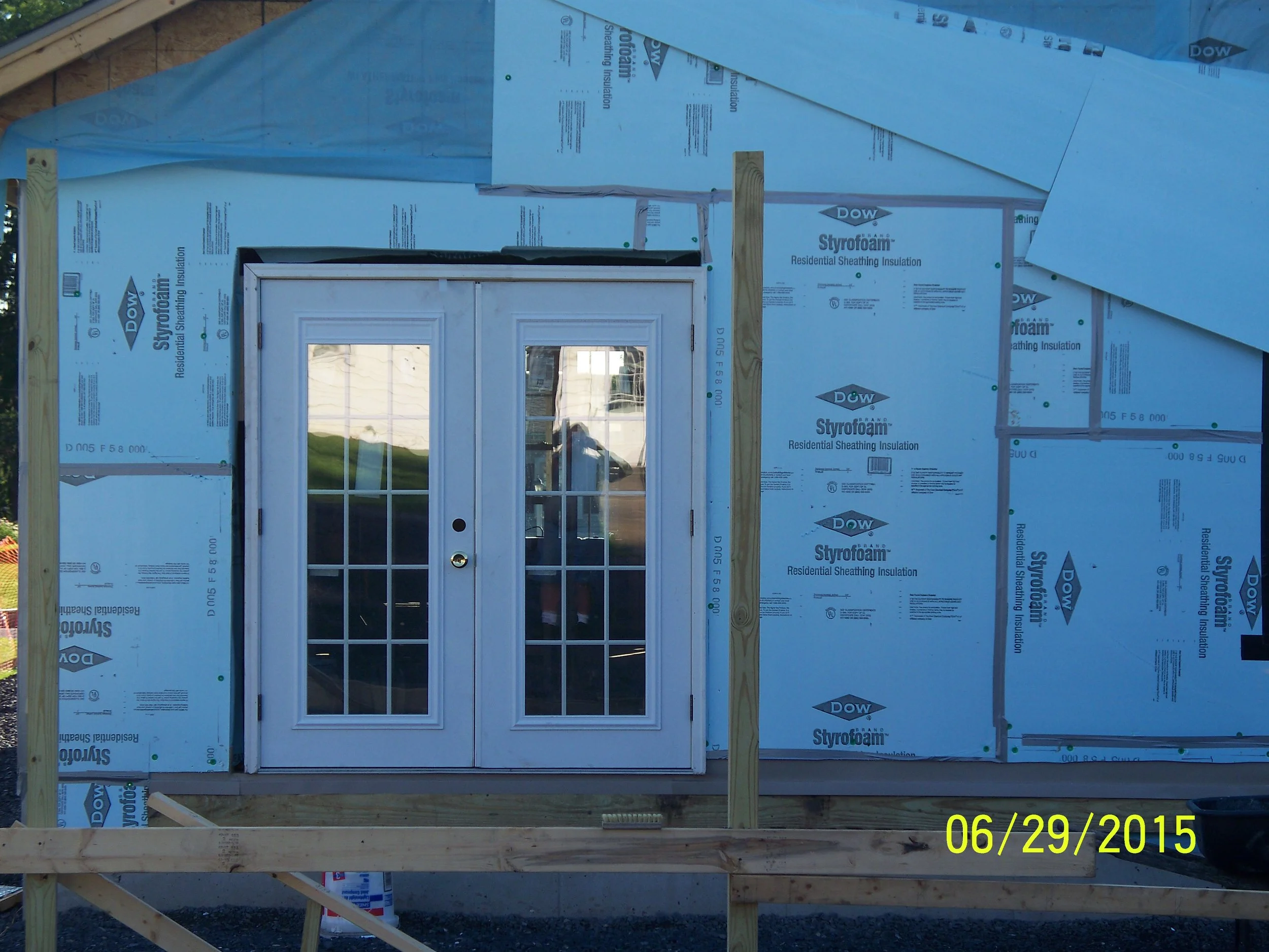 Construction site with a double glass door installed and wooden framing in progress, covered with Styrofoam insulation sheets.