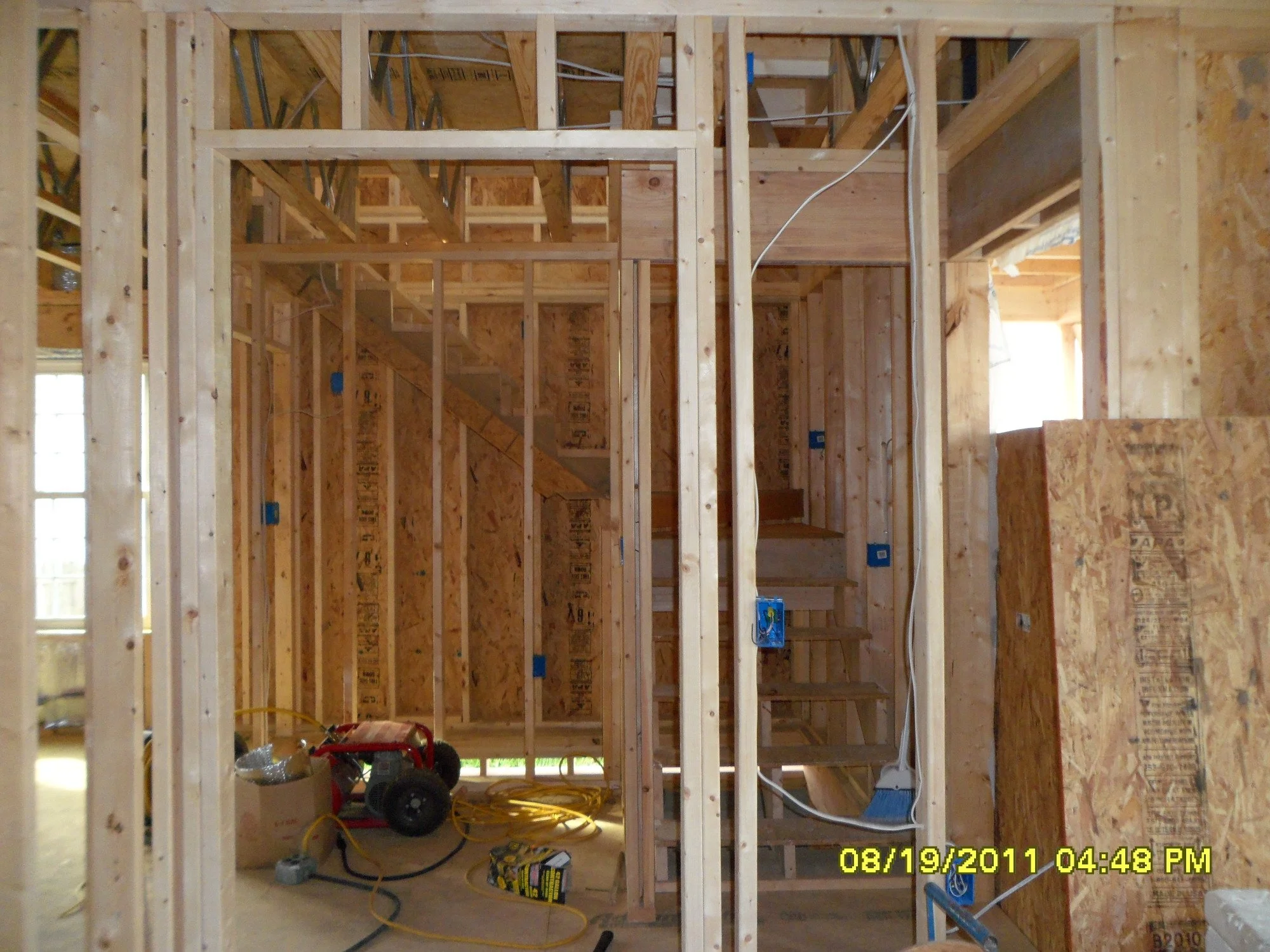 Interior view of a house under construction, showing wooden framing, stairs, and electrical wiring.