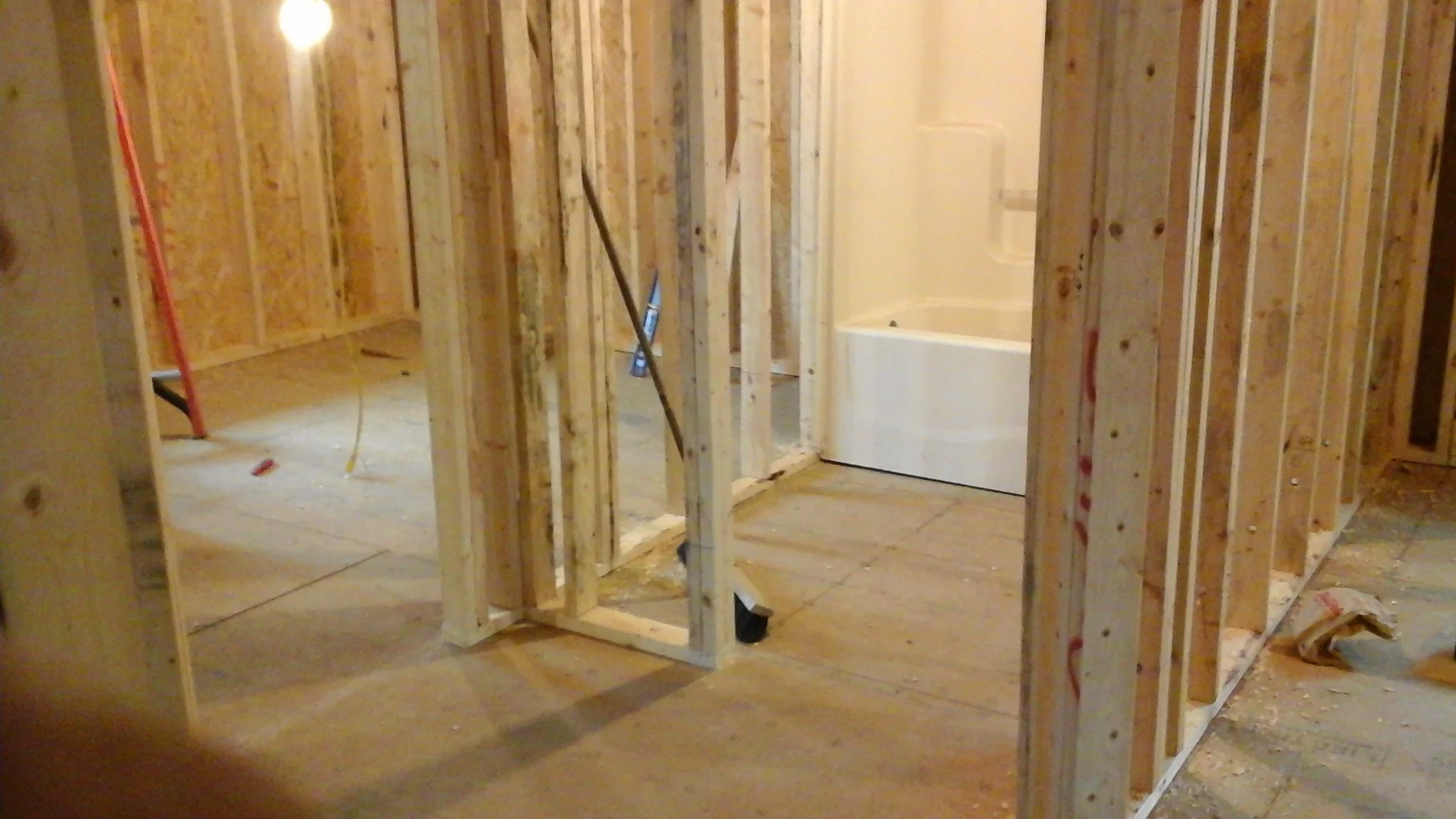 Interior view of a bathroom under construction, showing wooden framing, a bathtub in the corner, and construction tools and materials.