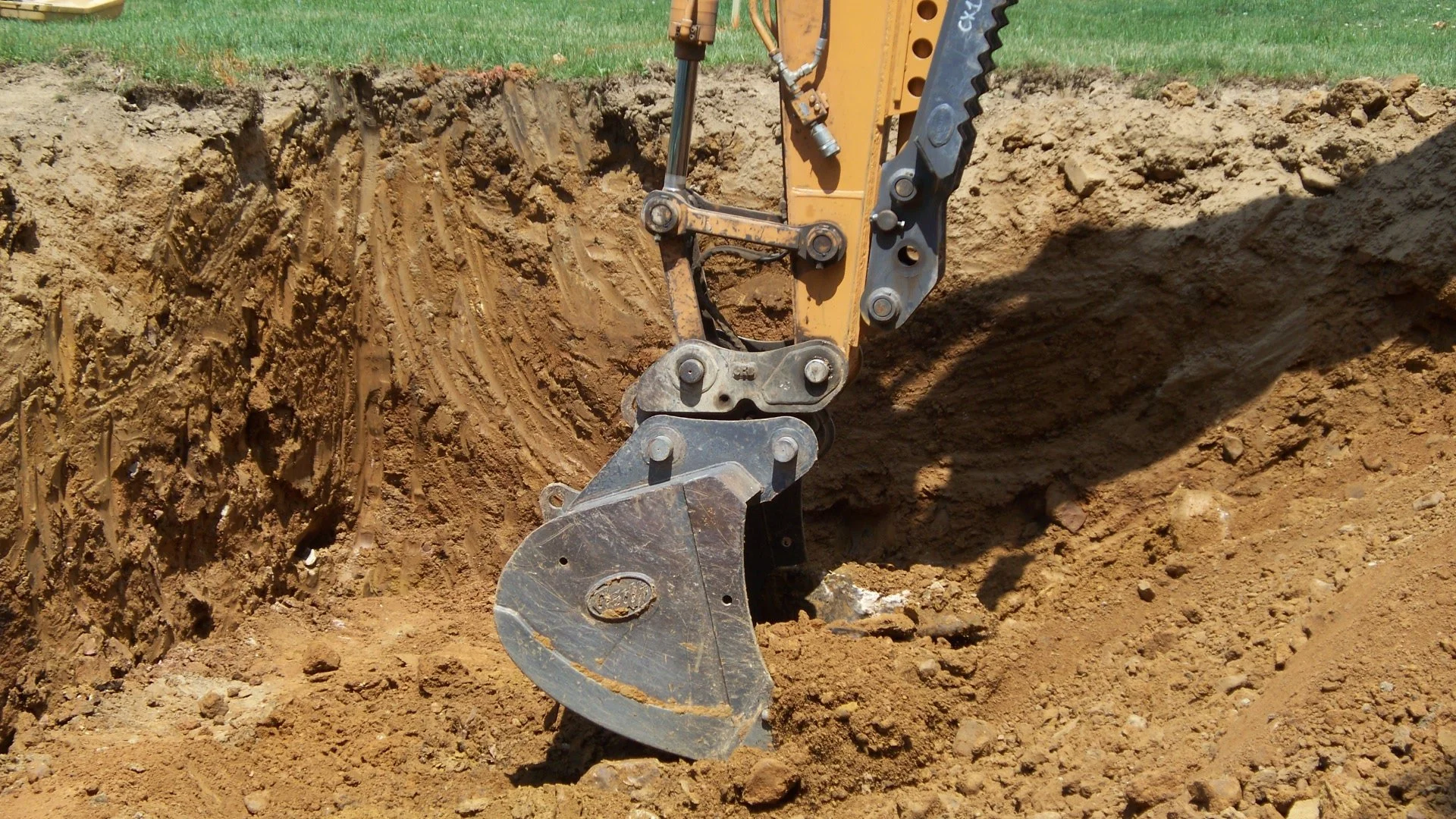 Close-up of a backhoe bucket excavator digging into dirt in an outdoor construction site.