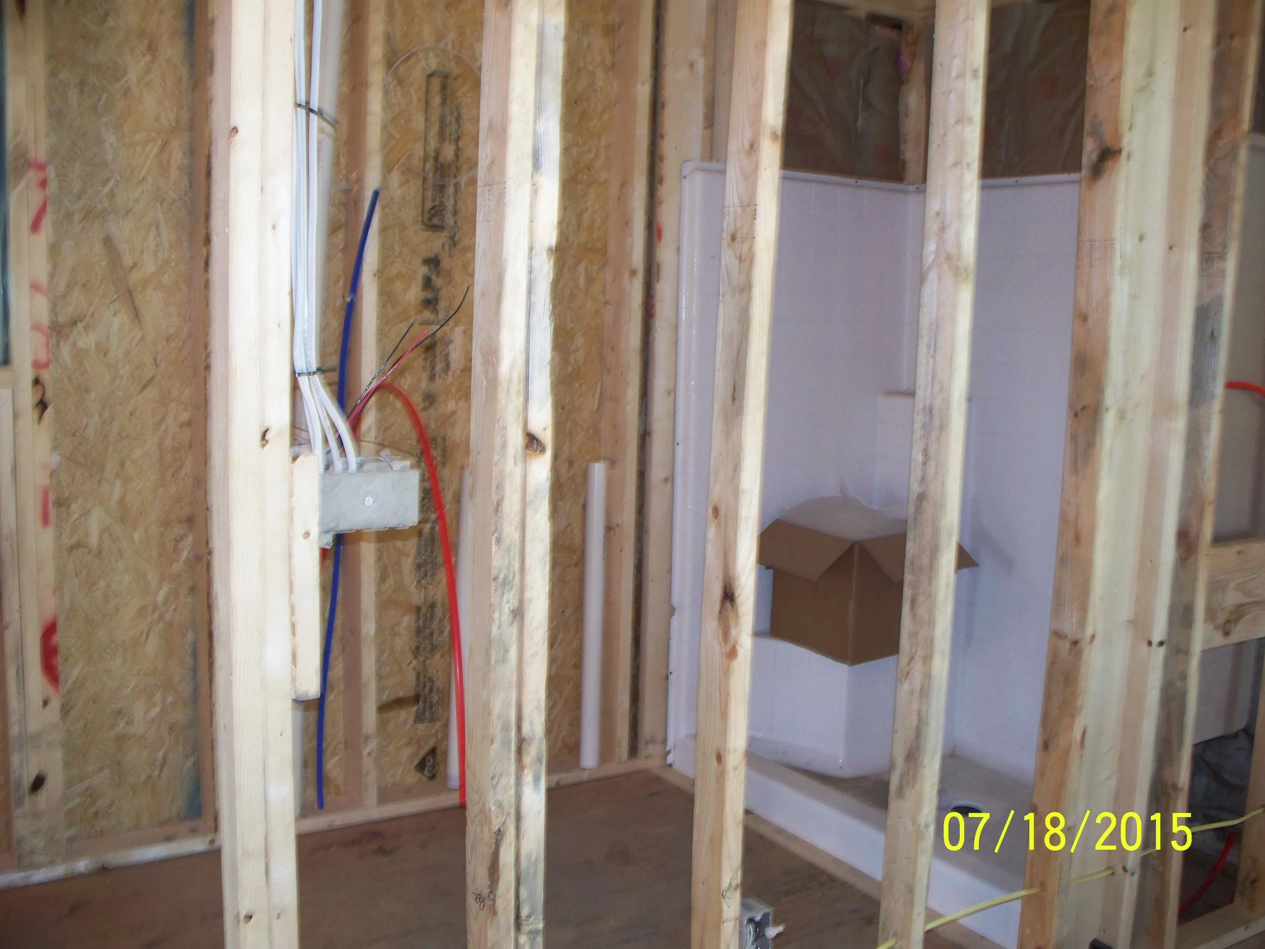 Interior view of a bathroom under construction, showing wooden framing, exposed electrical wiring, and the partially built toilet area with white tiles.