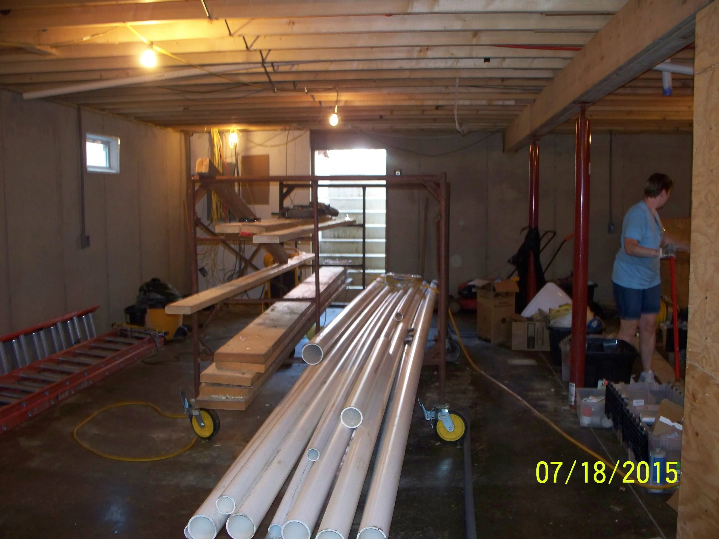 A woman working in a basement under construction, with pipes, tools, and building materials scattered around.