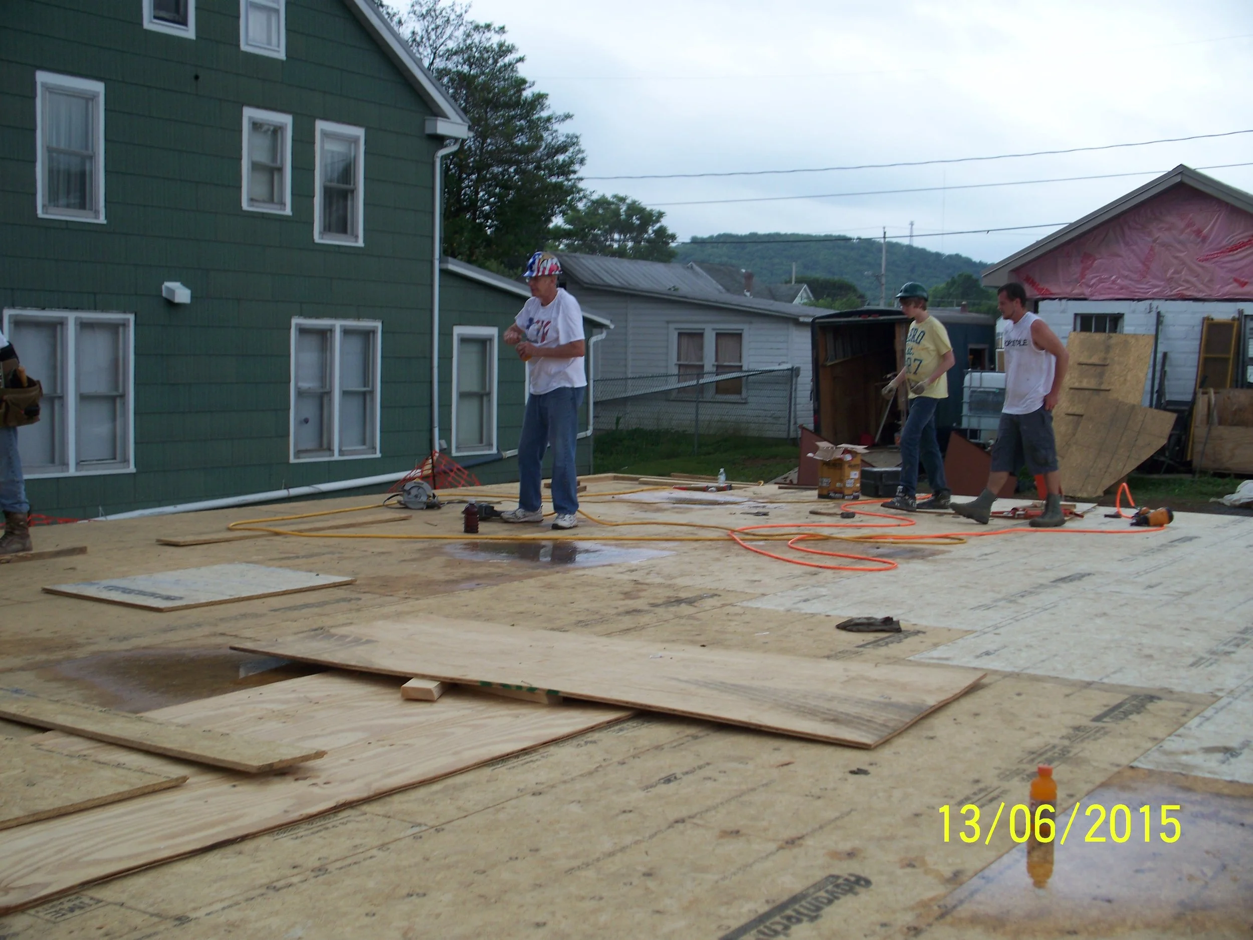 Four men working on a construction site for a building, with plywood sheets and construction tools scattered around.
