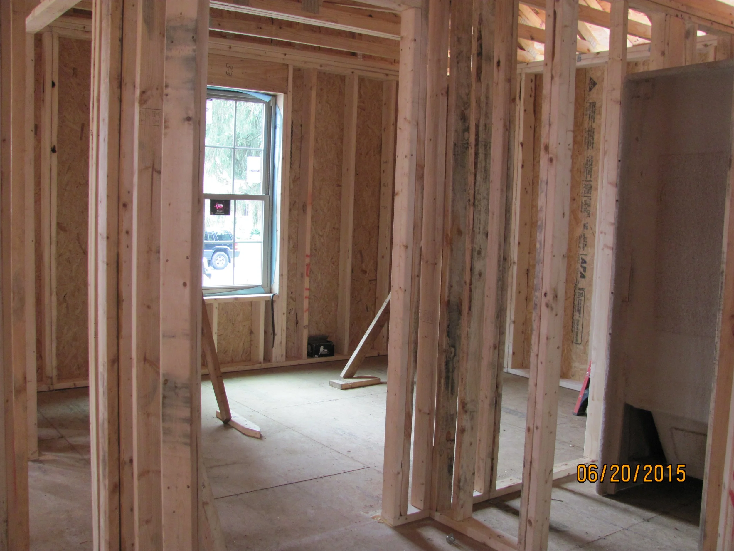 Interior view of a house under construction with exposed wooden framing, a window, and partial drywall installation.