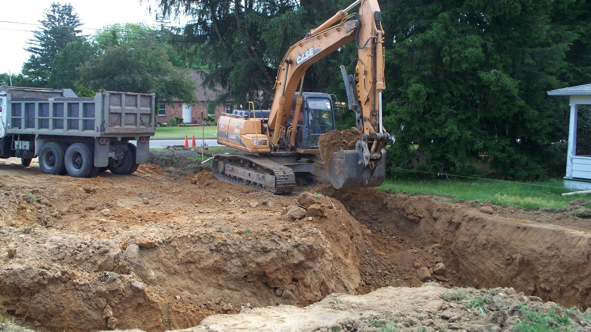 A construction site with a Case excavator digging a trench and a dump truck parked nearby.