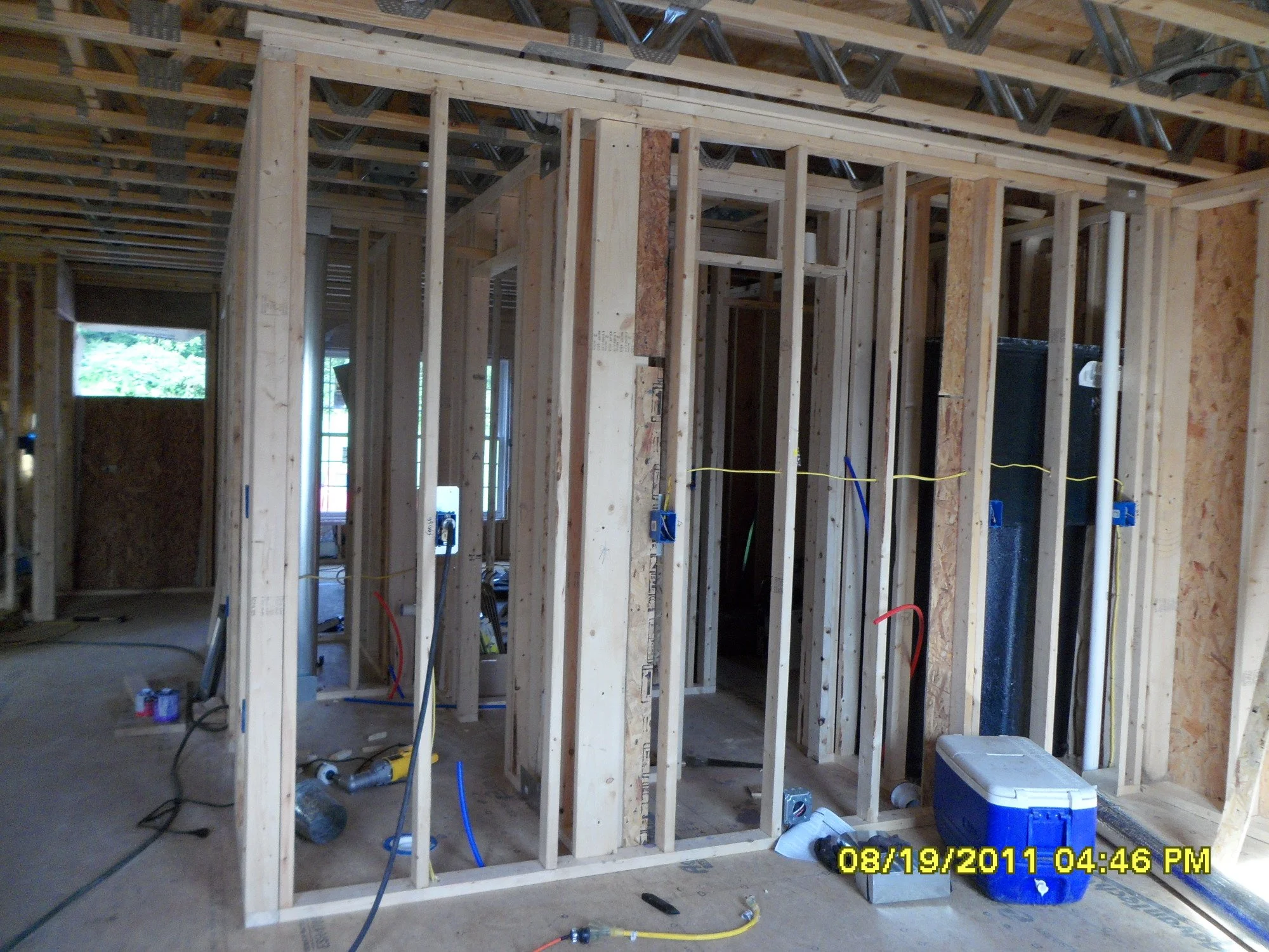 Interior framing of a house under construction, with wooden studs, electrical wiring, and construction tools on the floor.