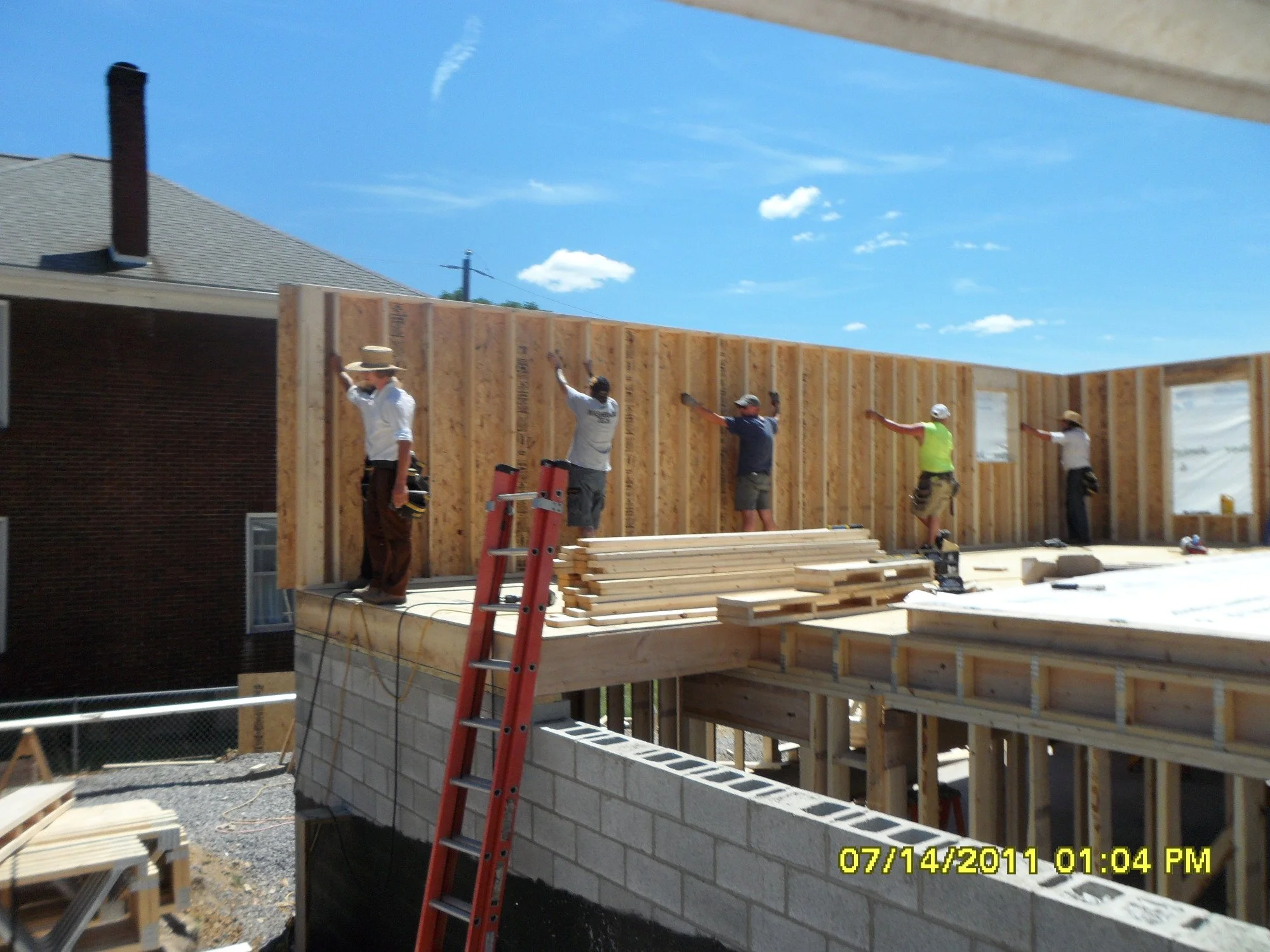 Construction workers installing wall framed with wood on a building under construction on a sunny day.