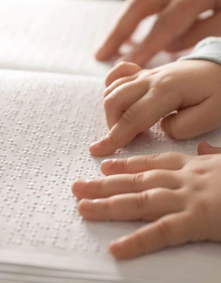 Close-up of a child's hand and another hand with fingers pointing on paper with Braille dots.
