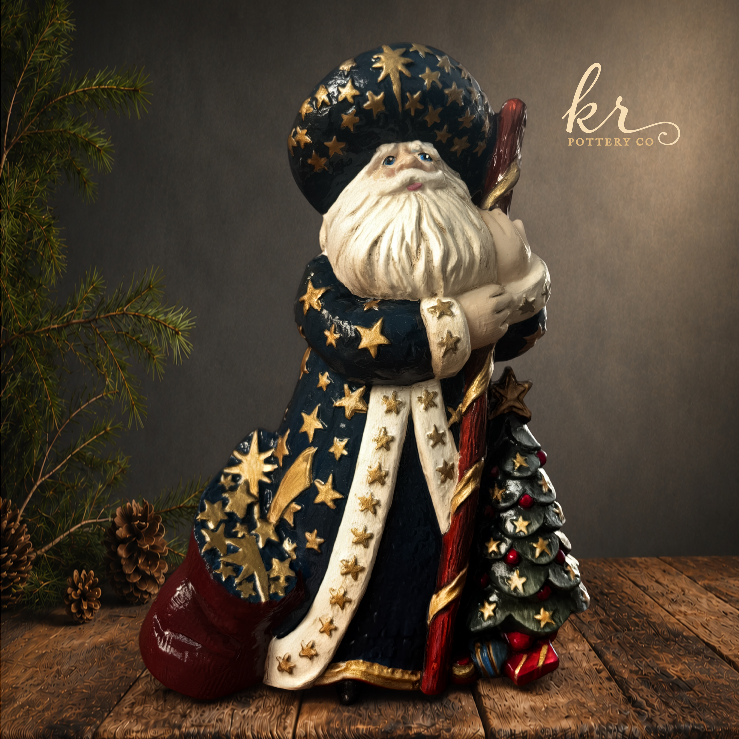 A decorative Santa Claus figurine wearing a dark blue hat with gold stars, holding a staff, surrounded by pinecones and pine branches, on a wooden surface.