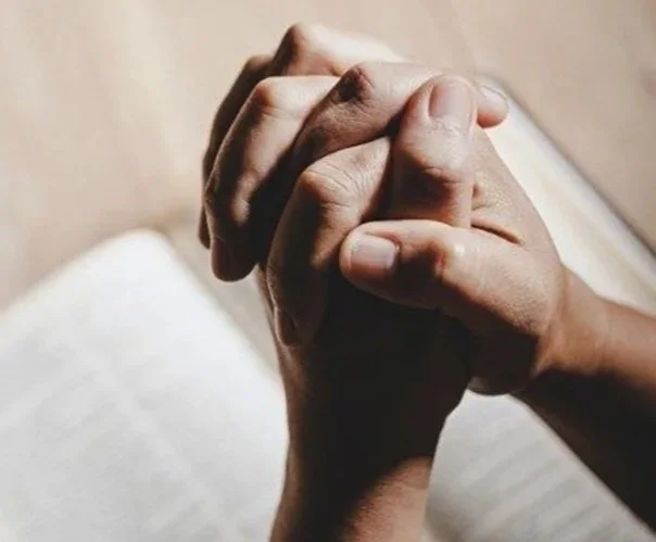 Close-up of two people holding hands in prayer or support, with a soft-focus background.