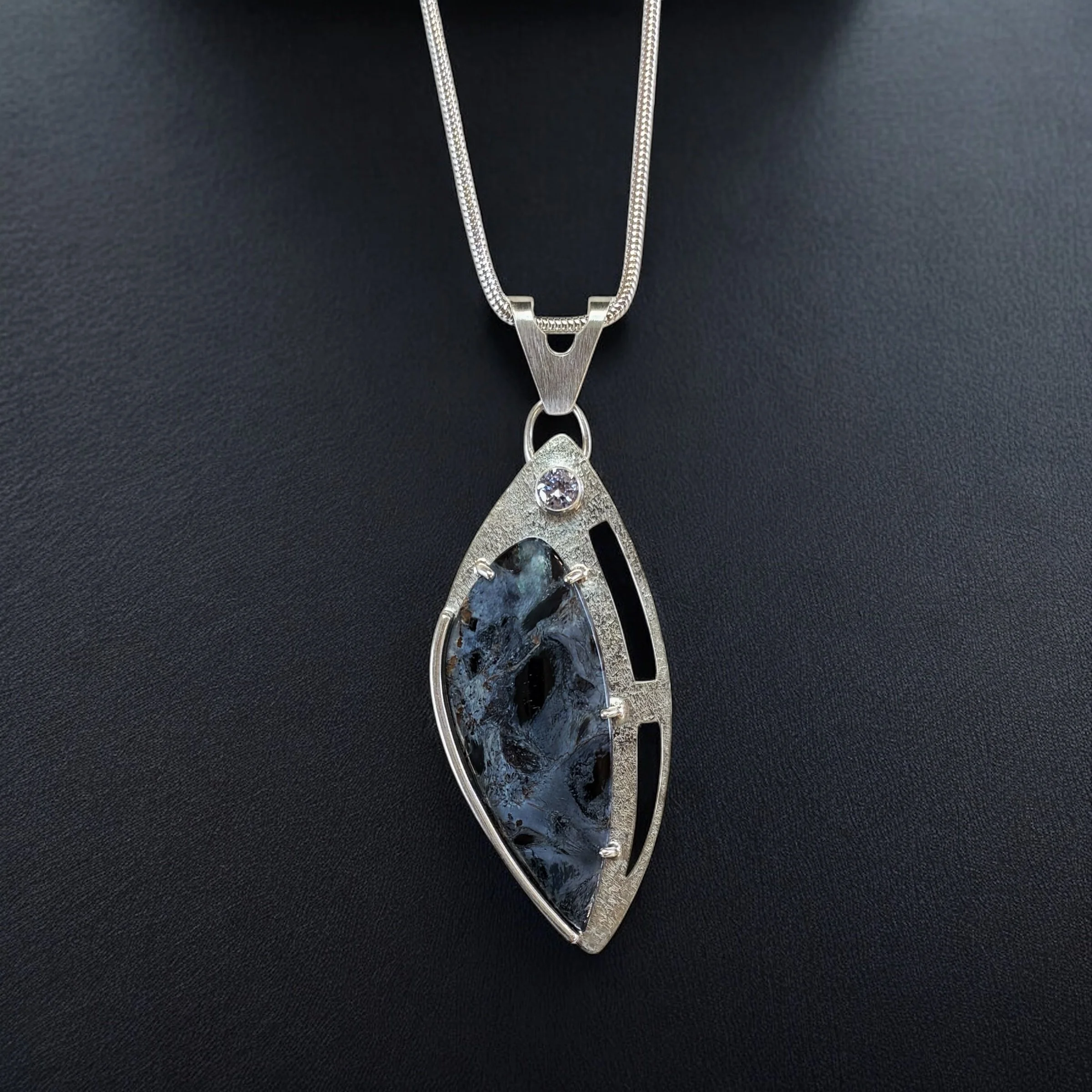 Pietersite in a sterling silver openwork pendant with a lavender cubic zirconia accent.