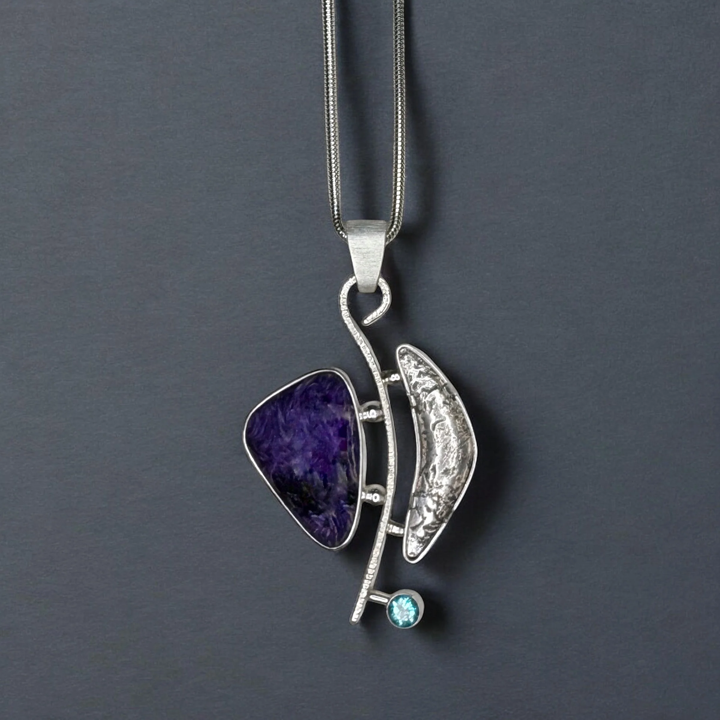Silver and charoite pendant with curved, sculptural form and blue apatite accent.