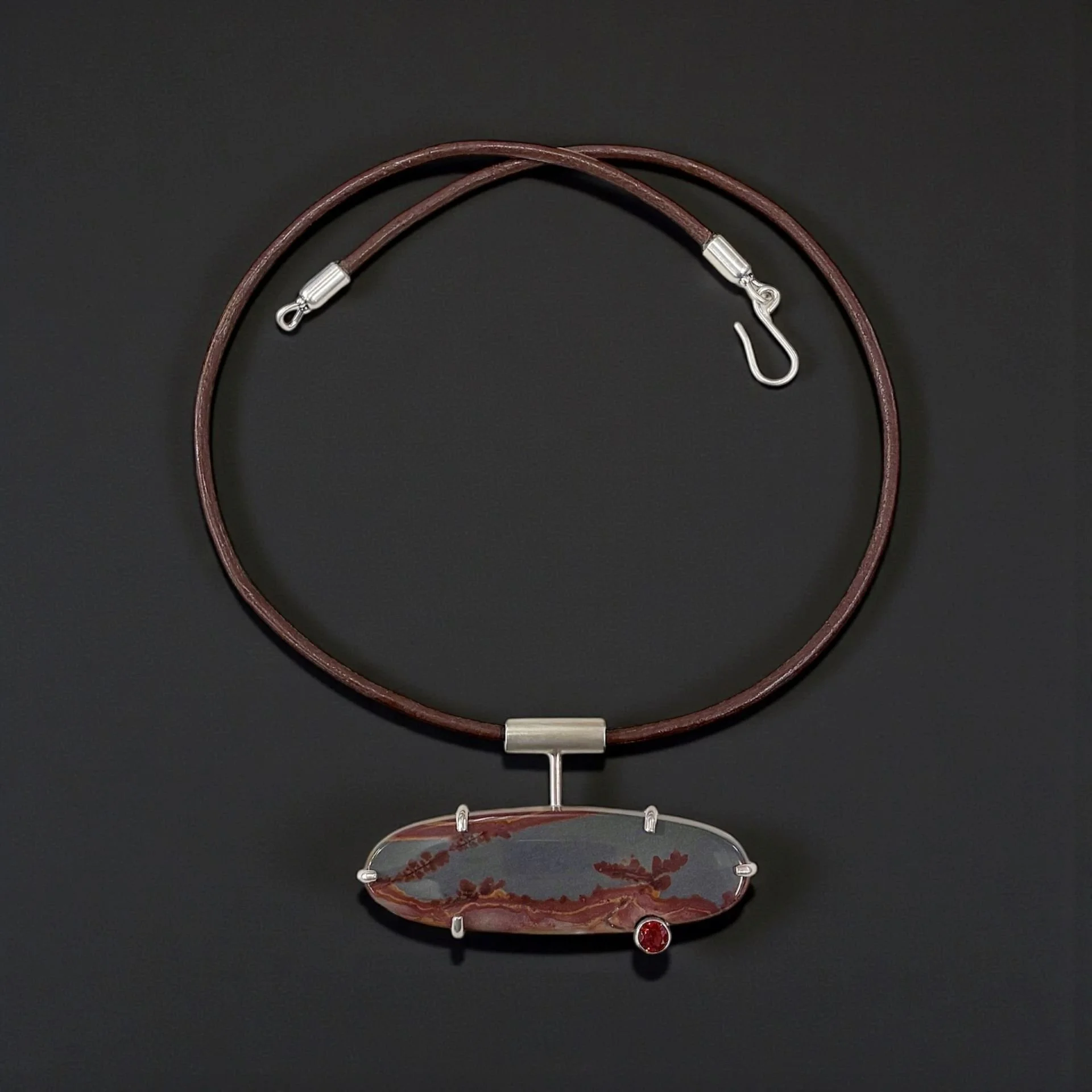 Desert jasper in a sterling prong‑set pendant with a garnet accent.