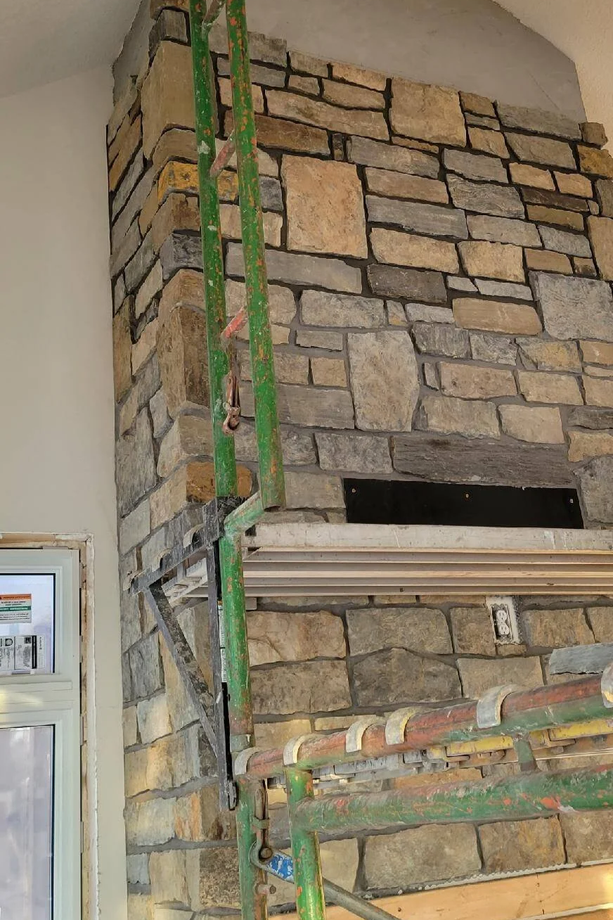 Close-up of a stone fireplace under construction with scaffolding and visible electrical outlets.