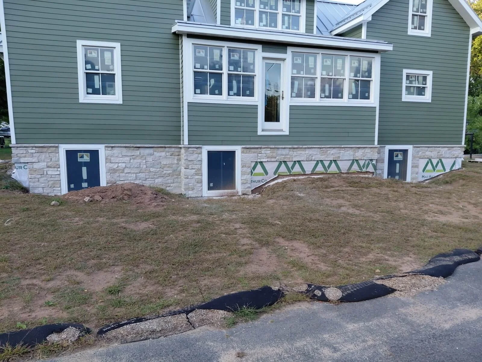 Construction site of a house with new siding and stone foundation. Dirt and black plastic edging along the sidewalk.