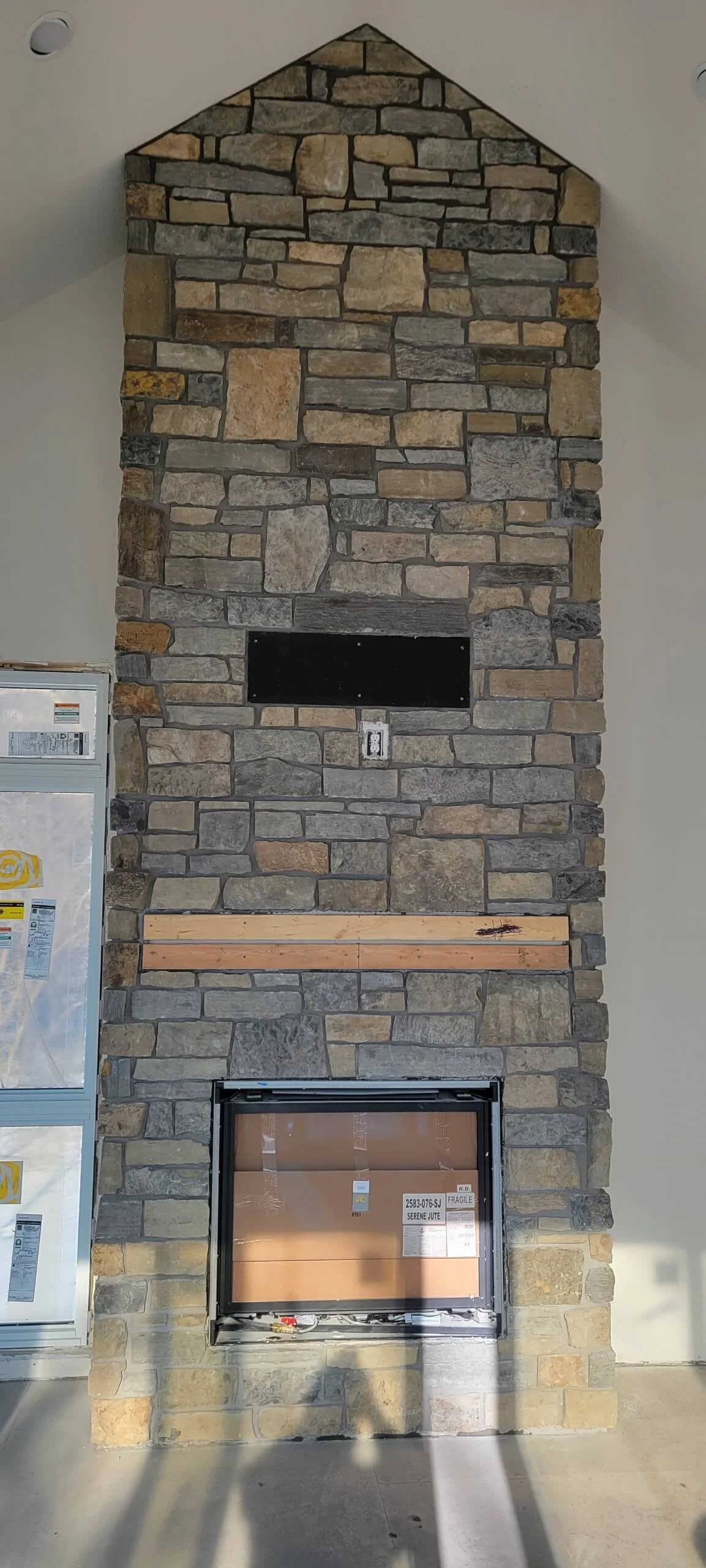 Stone fireplace with a rectangular opening at the bottom, a vent opening in the middle, and an unfinished wooden mantel.