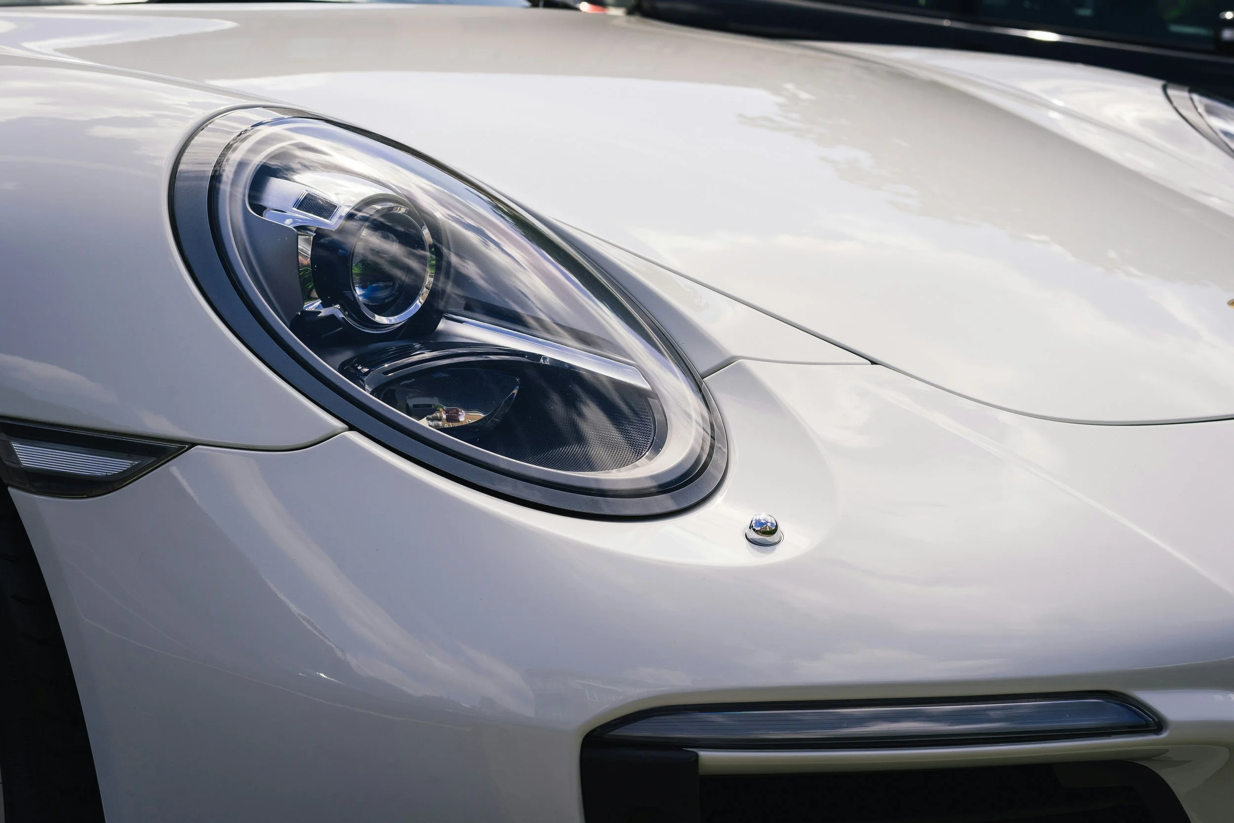 Le premier plan d'une voiture blanche, montrant la tête de phare avant gauche et une partie du capot.
