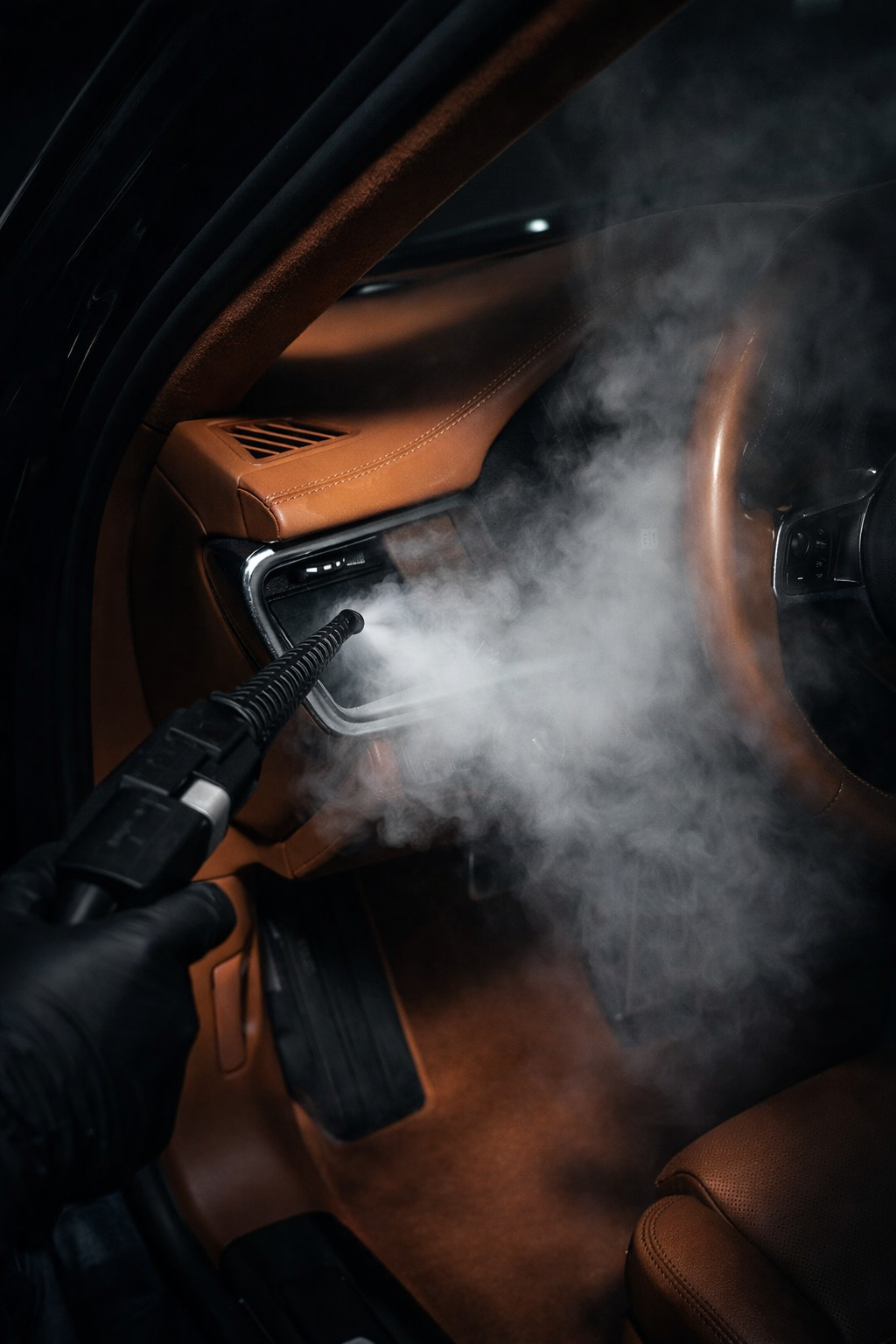 Une personne utilisant un appareil de nettoyage ou de désinfection dans l'habitacle d'une voiture, qui a un intérieur en cuir marron, avec de la vapeur ou de la fumée.