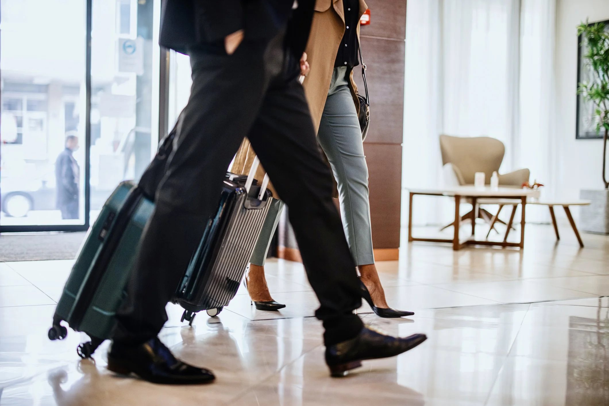 About Us, Eastside Christian Counseling in Kirkland, WA, People walking with rolling suitcases in a hotel lobby or airport. The focus is on their legs and suitcases, with furniture and a large window in the background.