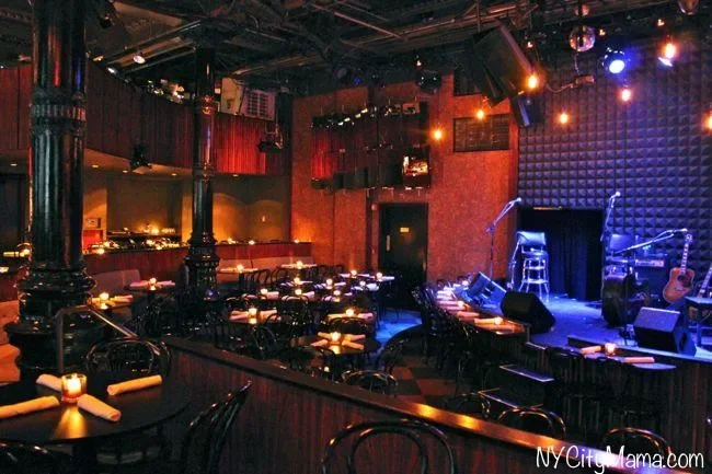 Empty nightclub or live music venue with a stage, musical instruments, and seating with tables and candles.