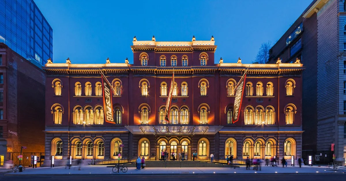 A historic building illuminated with yellow lights at dusk, with banners displaying "BID
