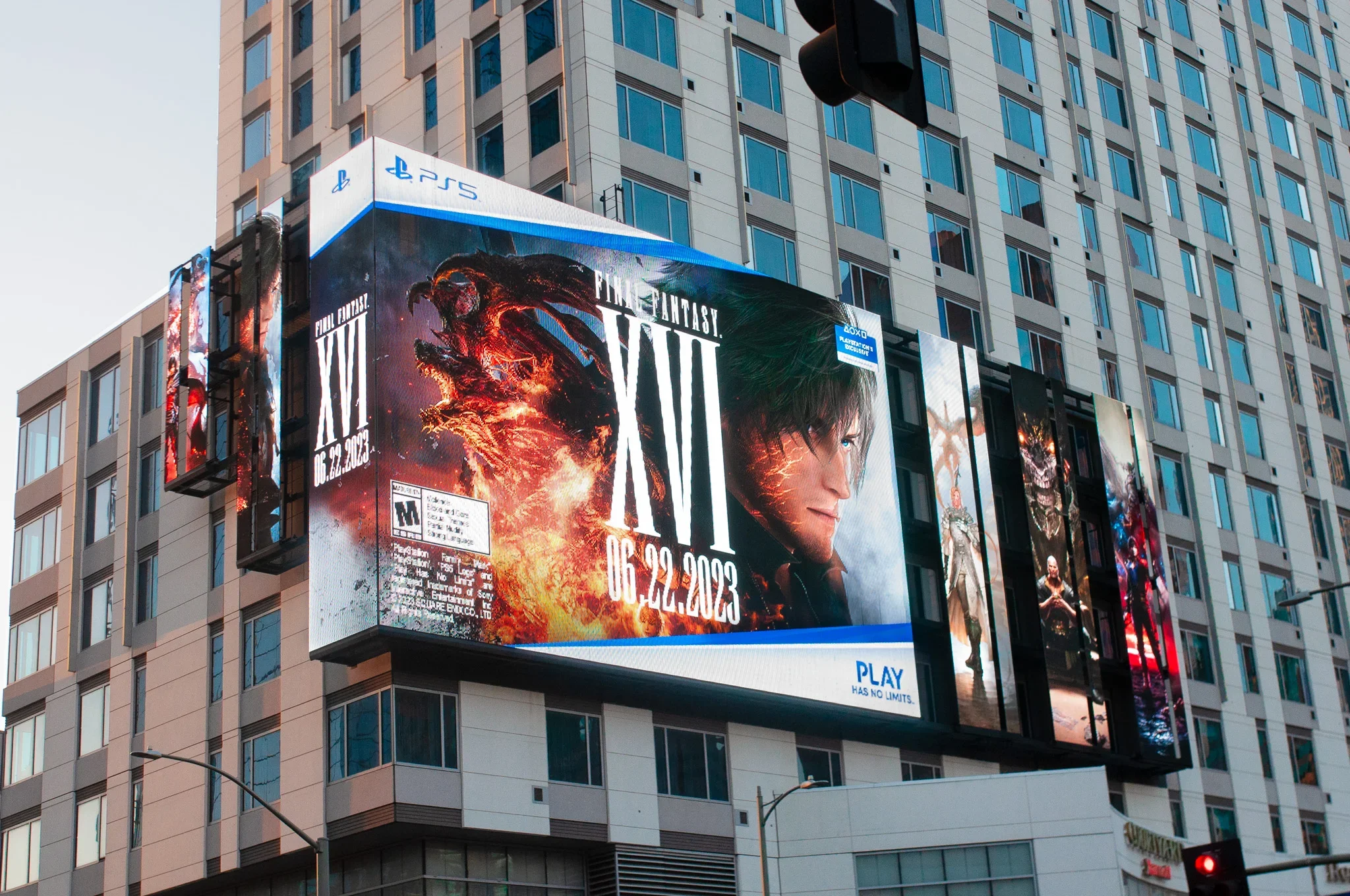 Digital billboards on a modern high-rise building advertising a video game called Final Fantasy VII. The billboard displays fiery imagery and a close-up of a male character's face.