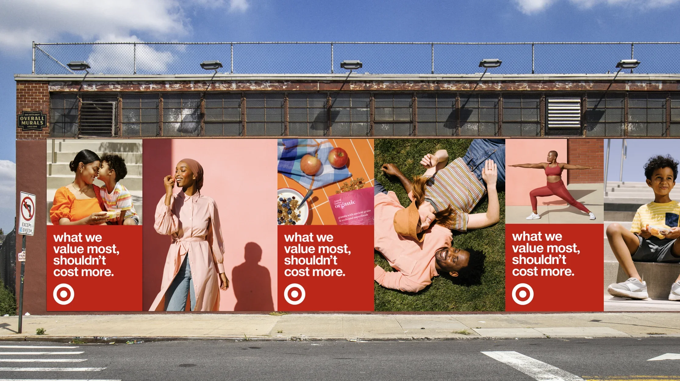 A billboard featuring diverse people and text about value and cost, with images including a mother and child, a woman smiling and holding an apple, a woman lying on grass, a woman in yoga pose, and a young boy eating. The billboard is on a brick building under a blue sky.