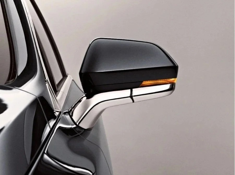 Close-up of a black side mirror on a modern car with a neutral background.