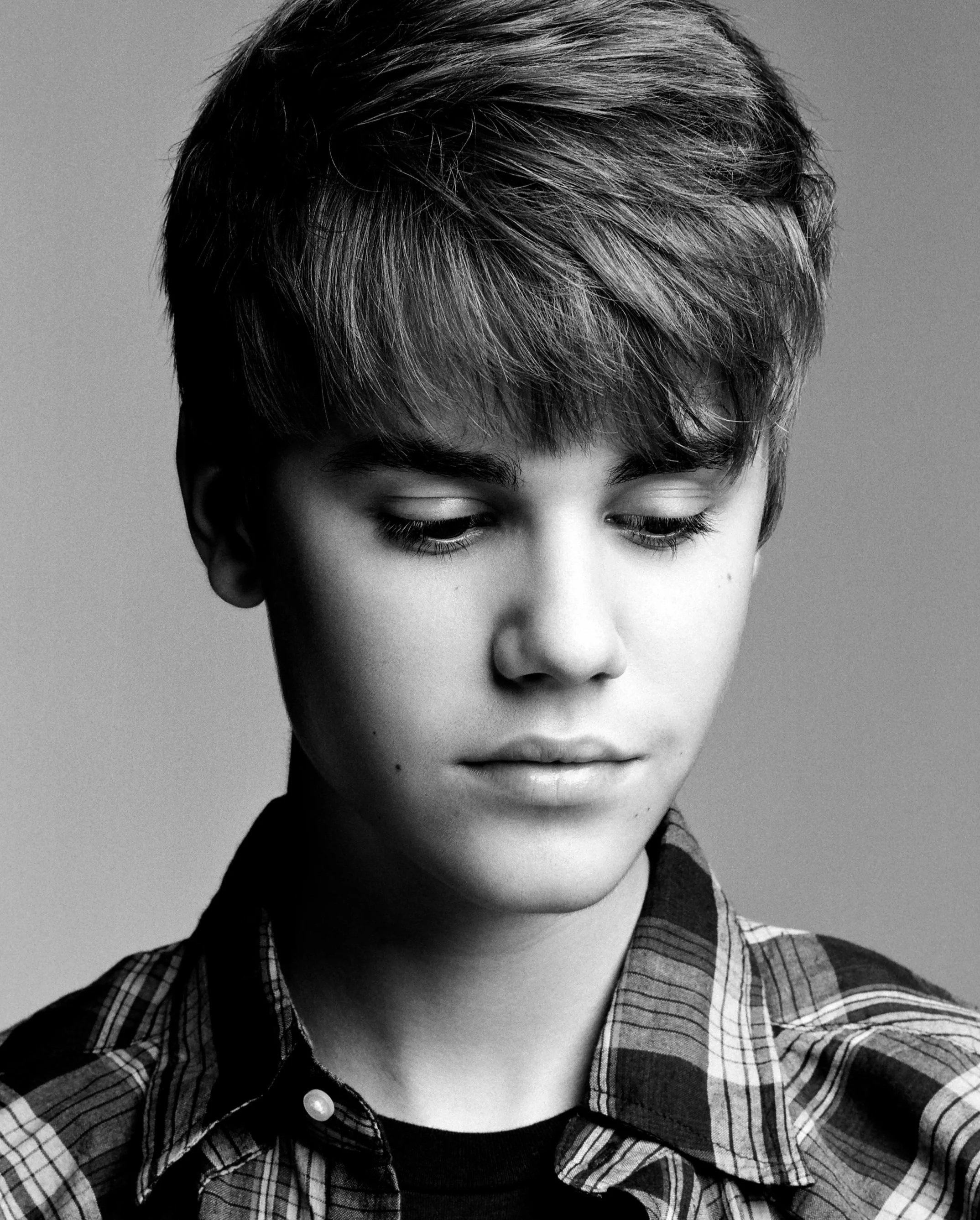 Black-and-white photo of a person with short, layered hair wearing a plaid shirt with a collar, looking downward.
